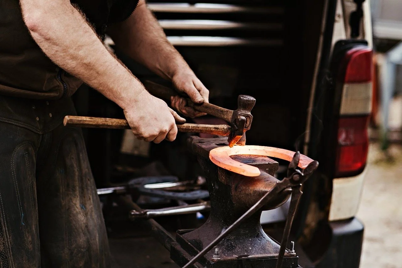 Blacksmith shaping a horseshoe on an anvil with a hammer and chisel.
