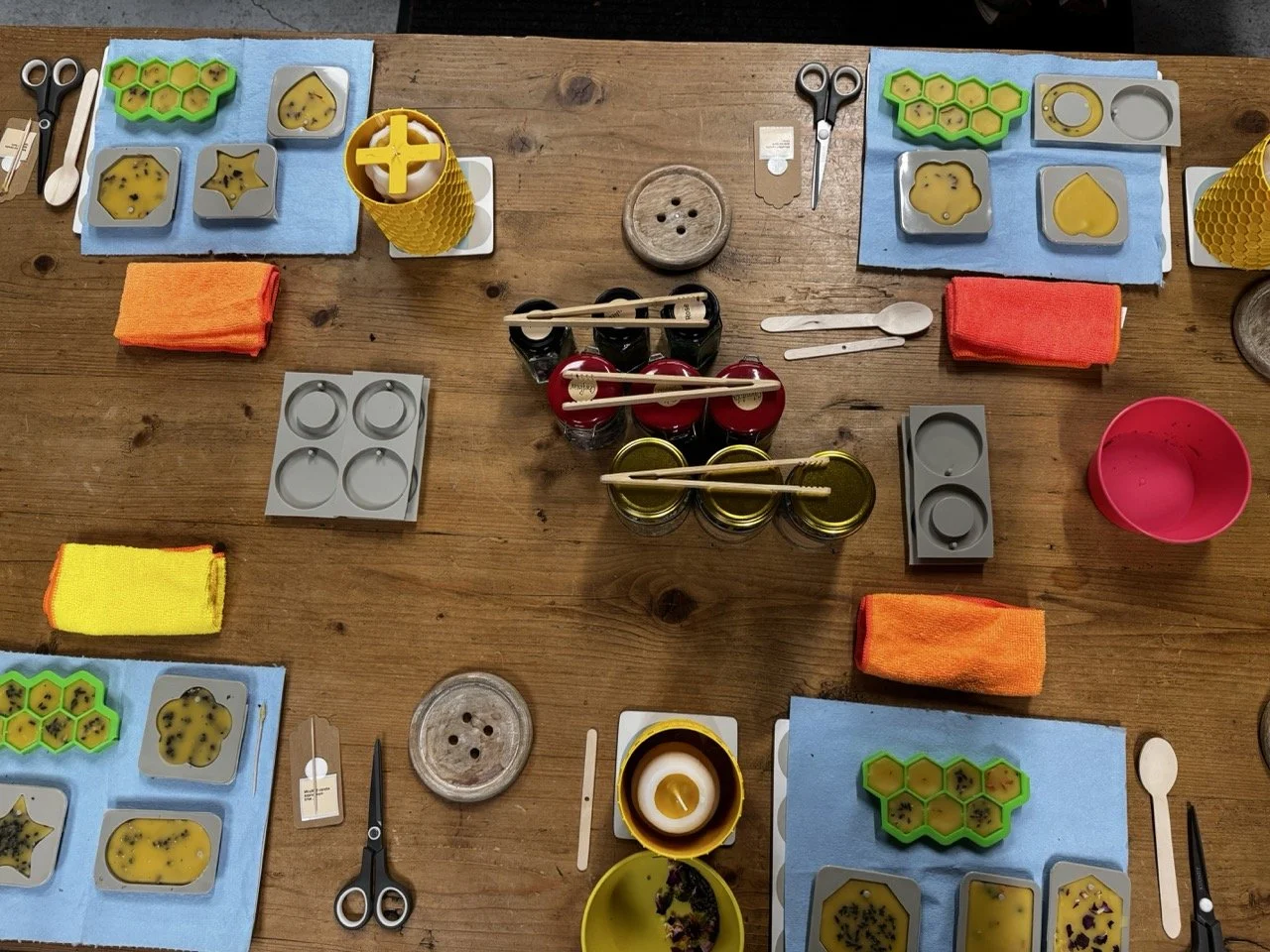Table set for a bee-themed activities with honeycomb-shaped containers, jars of honey, colorful cloths, scissors, spoons, and other small supplies for honey-related tasting or crafts.