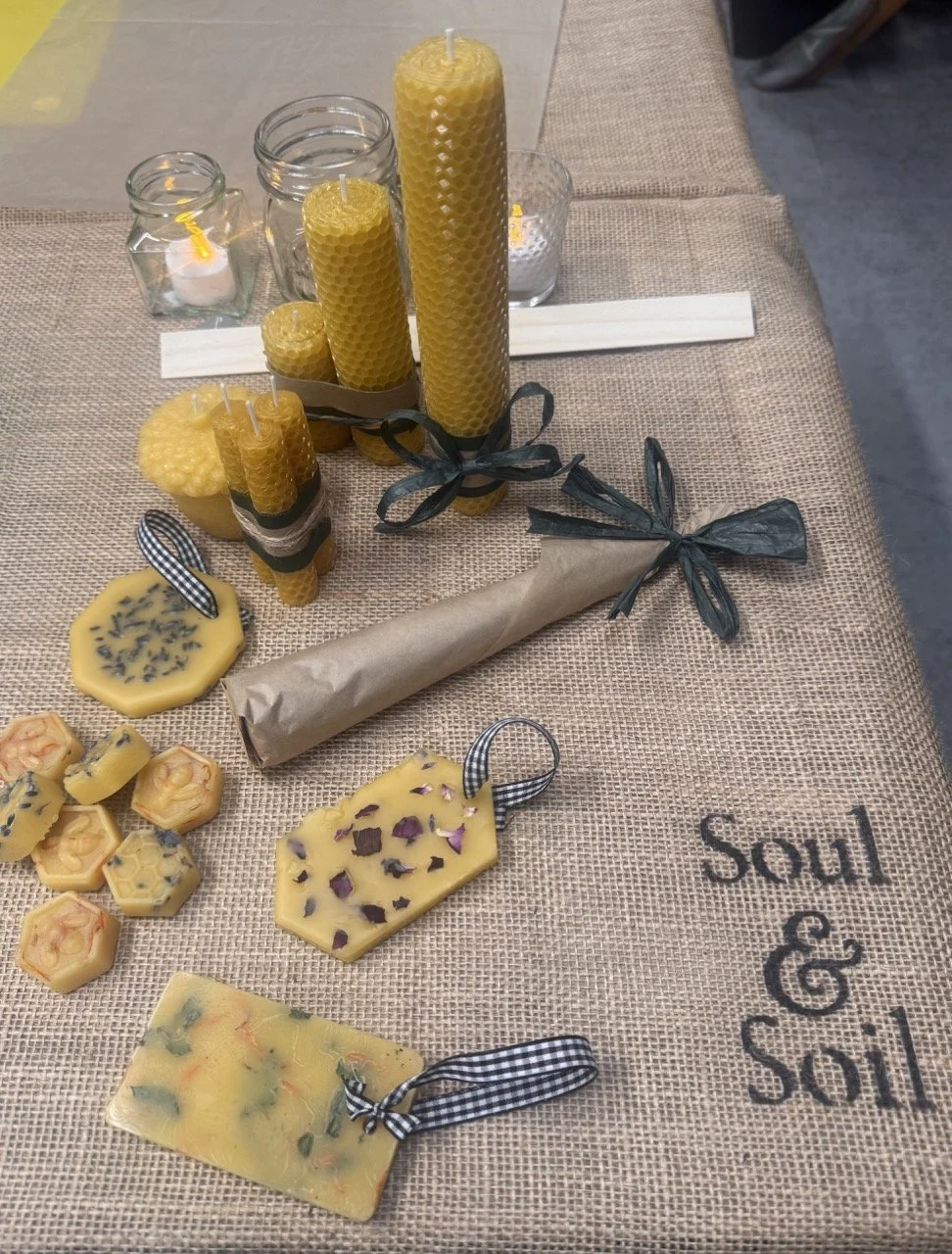 Arrangement of beeswax candles and decorative soaps on a burlap tablecloth with the word 'Soul' embroidered on it.