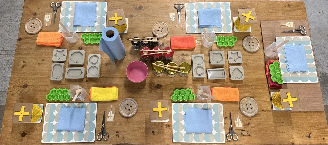 A top-down view of a wooden table set for five people, with crafting supplies, fabric, and tools arranged at each place.