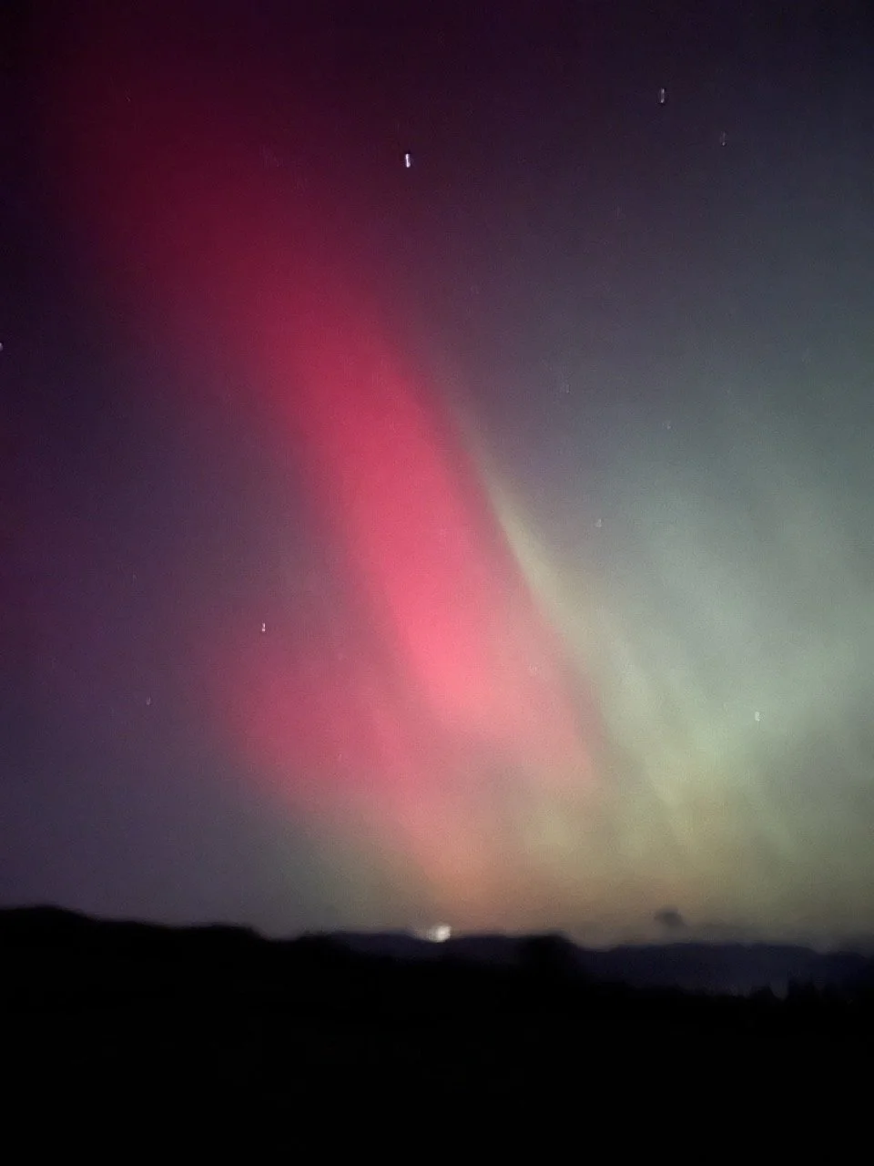 Northern lights (aurora borealis) with pink and green hues over a dark landscape at night.