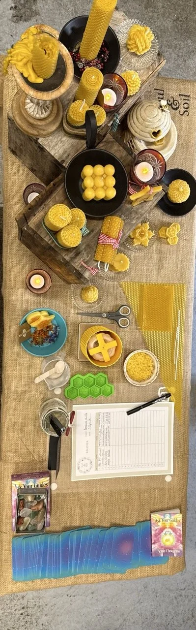 An overhead view of a table setup for beeswax candle making, featuring candles, honeycomb, scissors, wax sheets, a green honeycomb mold, and guiding materials.