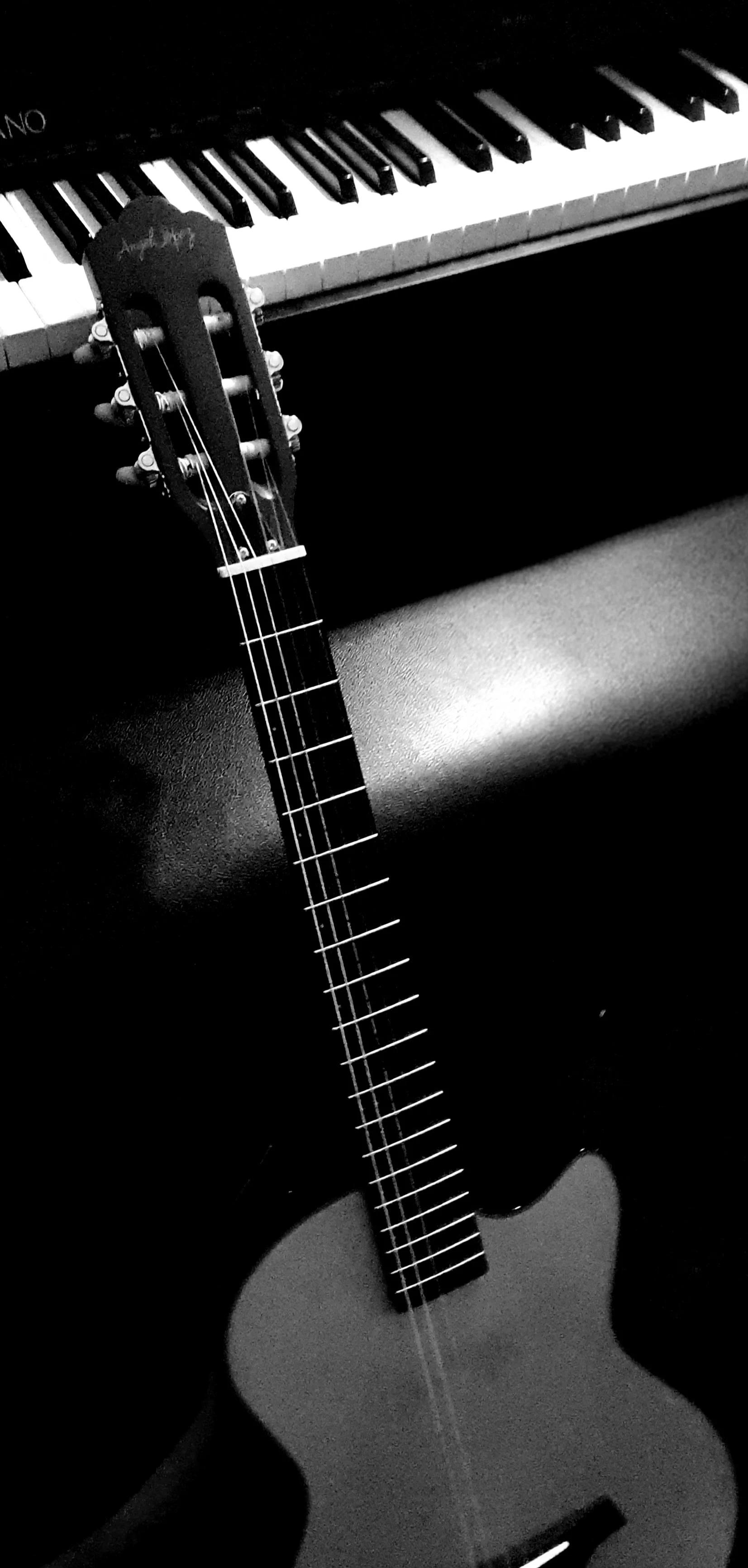 Black and white photo of an classical guitar leaning against a piano keyboard.