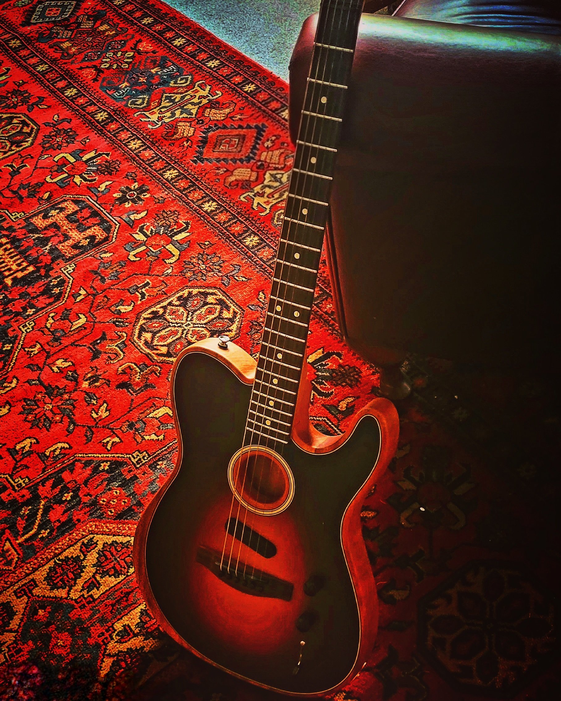 An electric guitar resting on a Persian-style red and black patterned rug.
