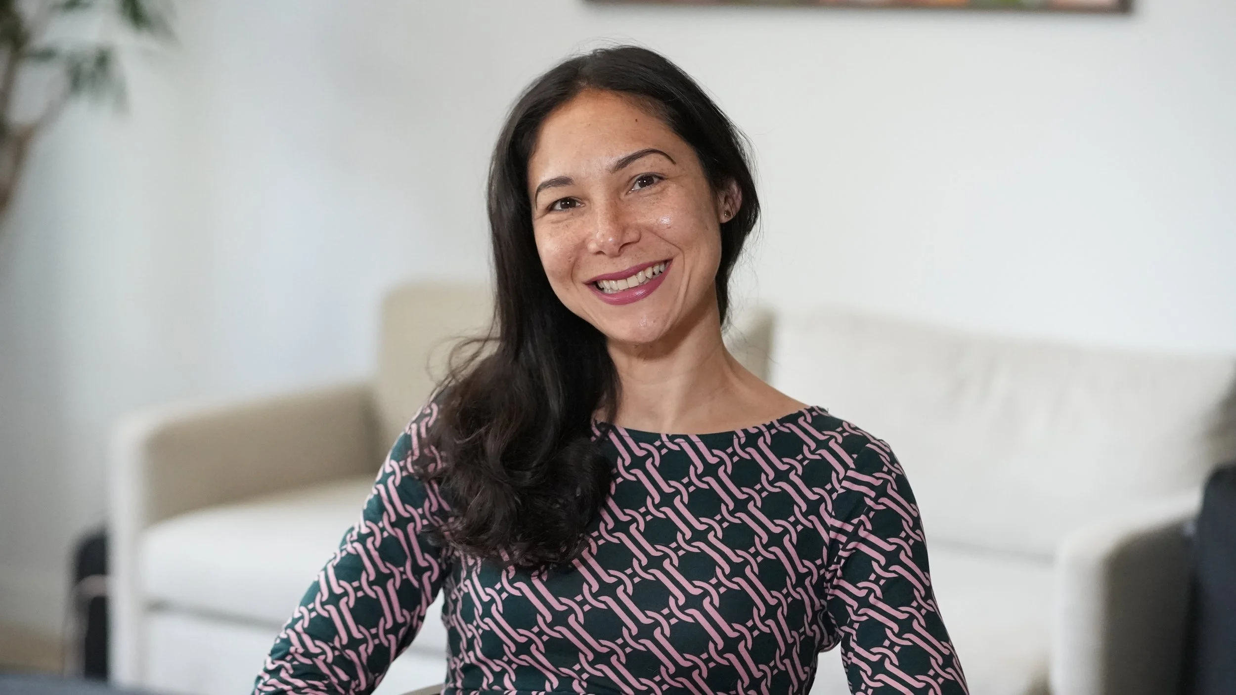 A picture of Mindy Simon. She has long black hair and a patterned top and she is smiling