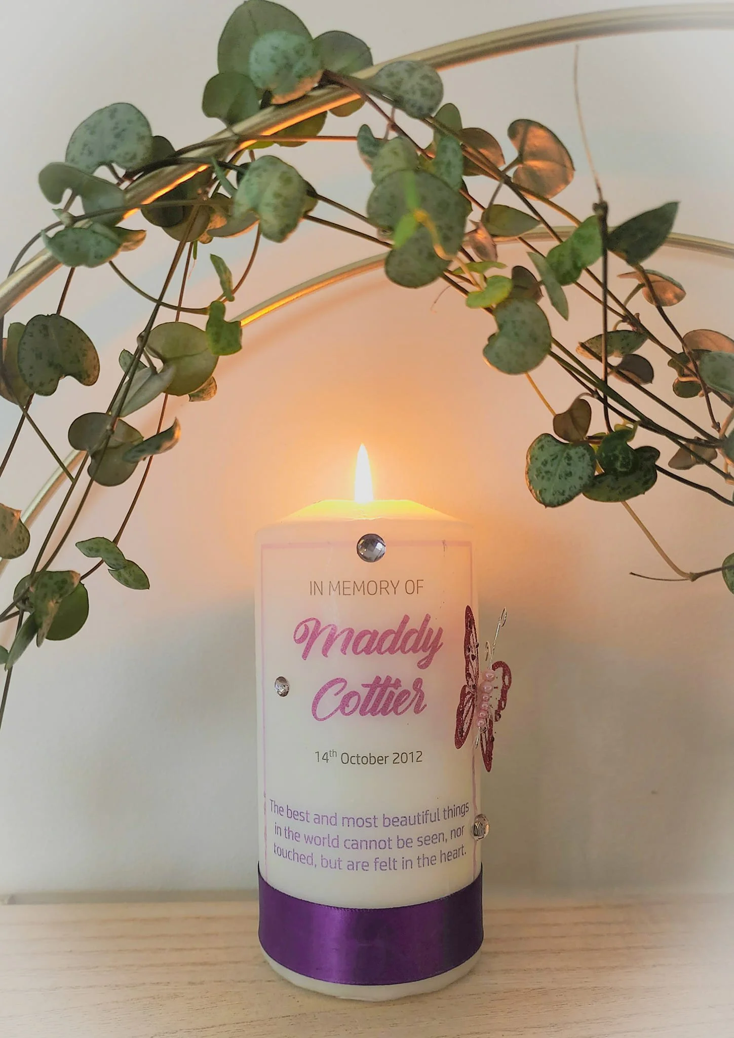 Lit memorial candle inscribed "In Memory of Maddy Cottier" with butterfly embellishment