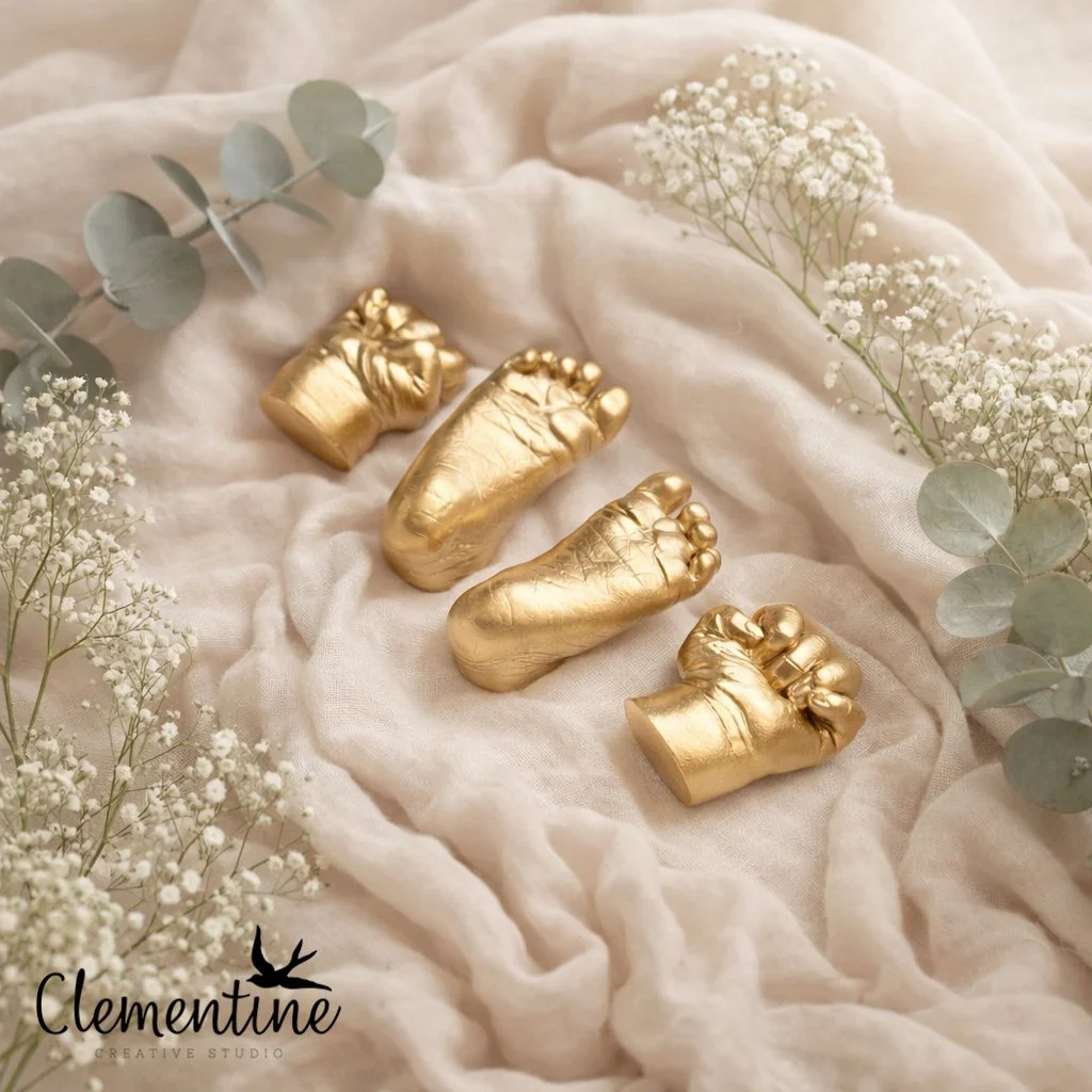 A gold baby hand and foot casting set arranged on soft linen fabric with white gypsophila and eucalyptus — a beautiful newborn keepsake by Clementine Creative Studio, New Zealand.