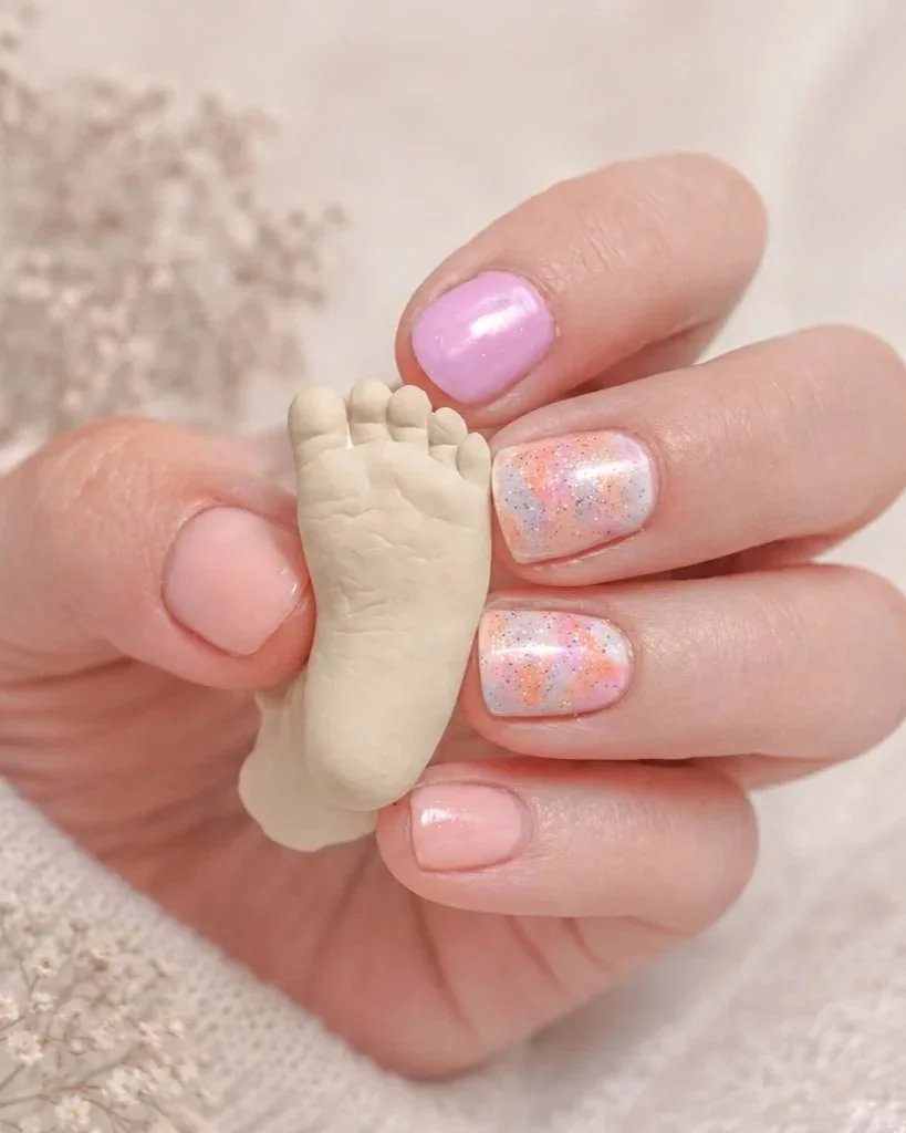A tiny white baby foot casting held gently in a mother's hand, surrounded by soft gypsophila — a delicate newborn keepsake by Clementine Creative Studio, New Zealand