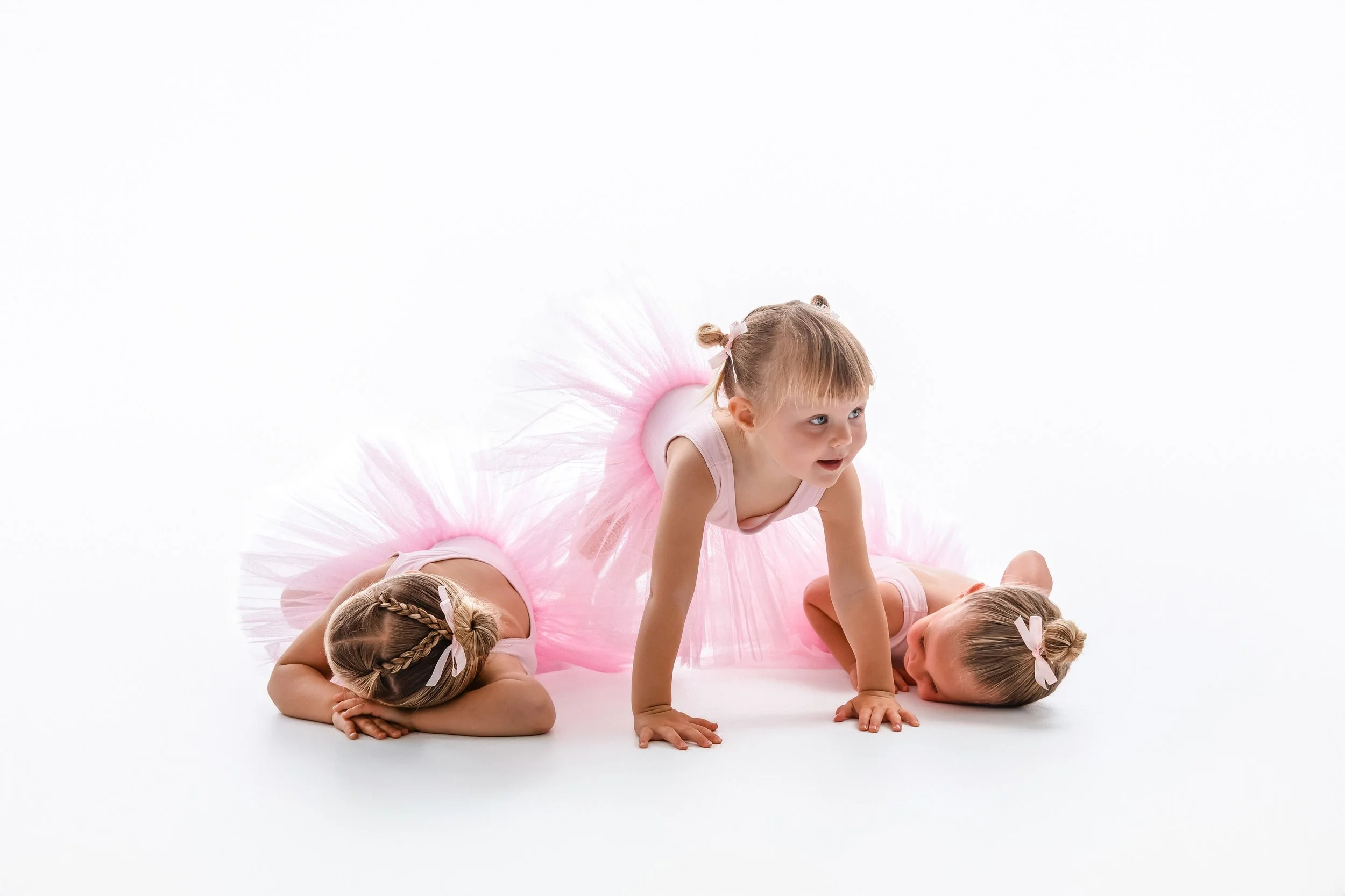 Children dressed as ballerinas practicing a dance pose on a white background.