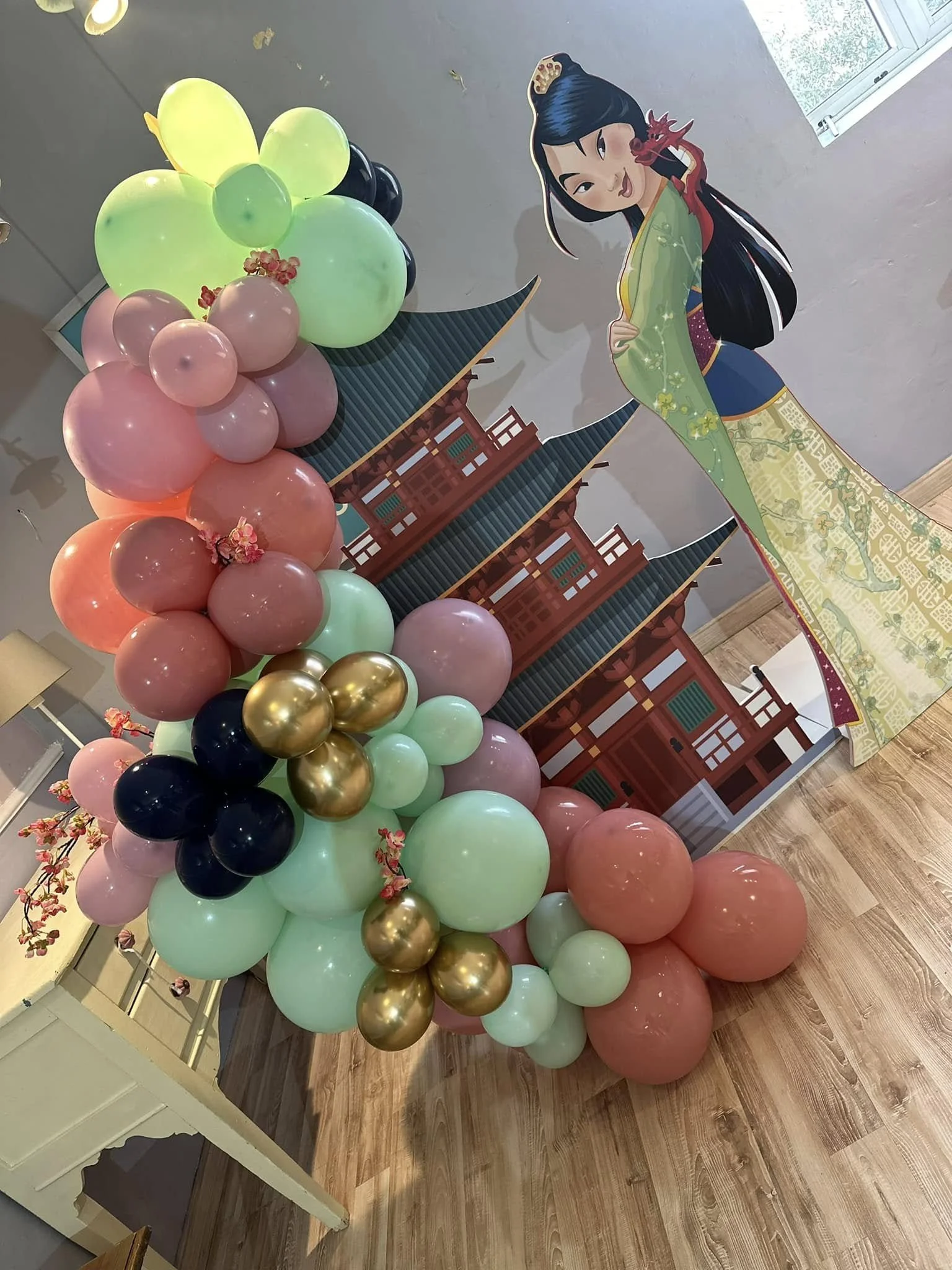 Colorful balloon temple with pink, green, black, and gold balloons, along with a backdrop featuring Mulan  and traditional Asian architecture elements.