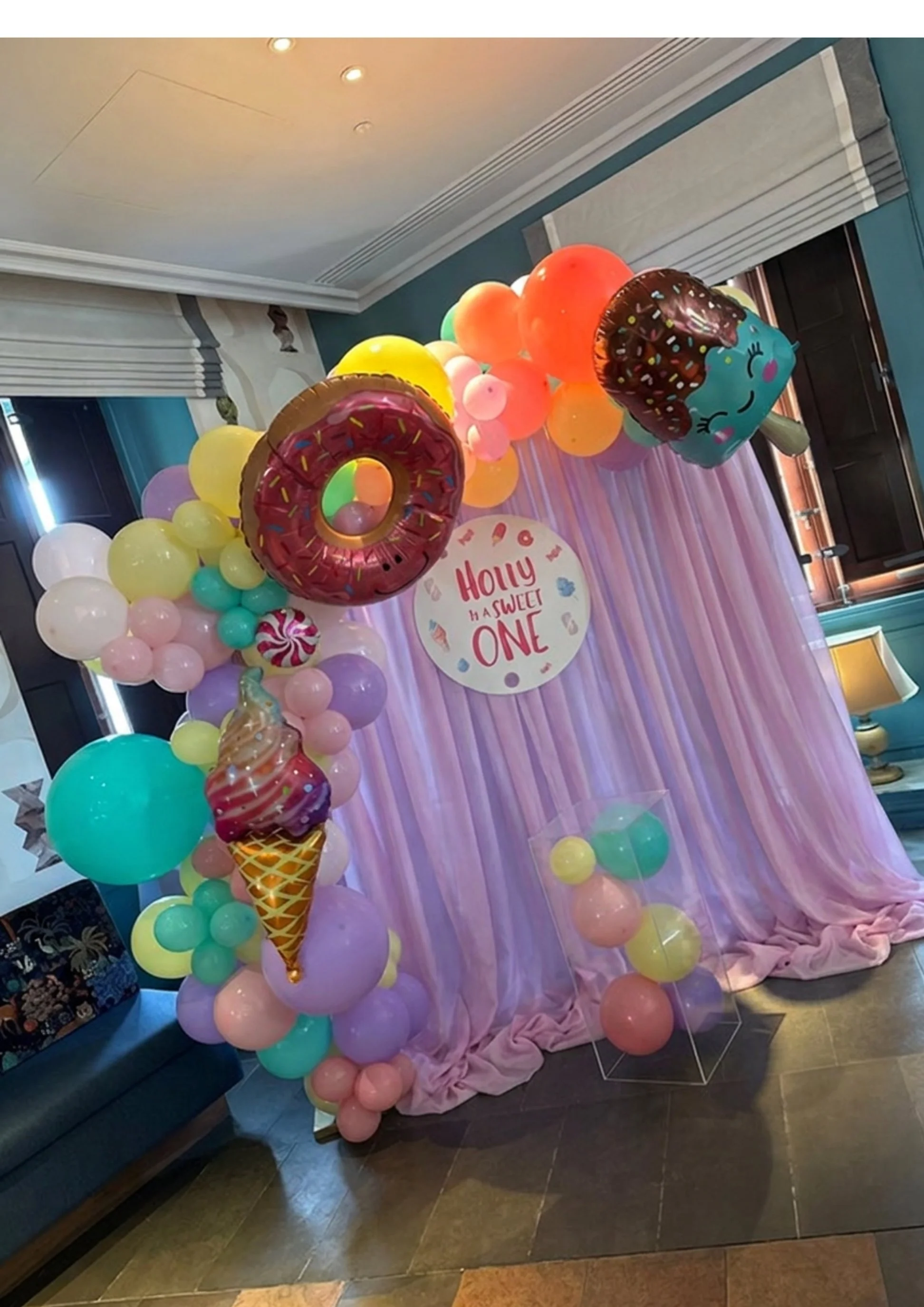 Colorful balloon arch with an ice cream cone balloon and a circular sign that reads 'Holly is a sweet one' at a birthday party decoration.