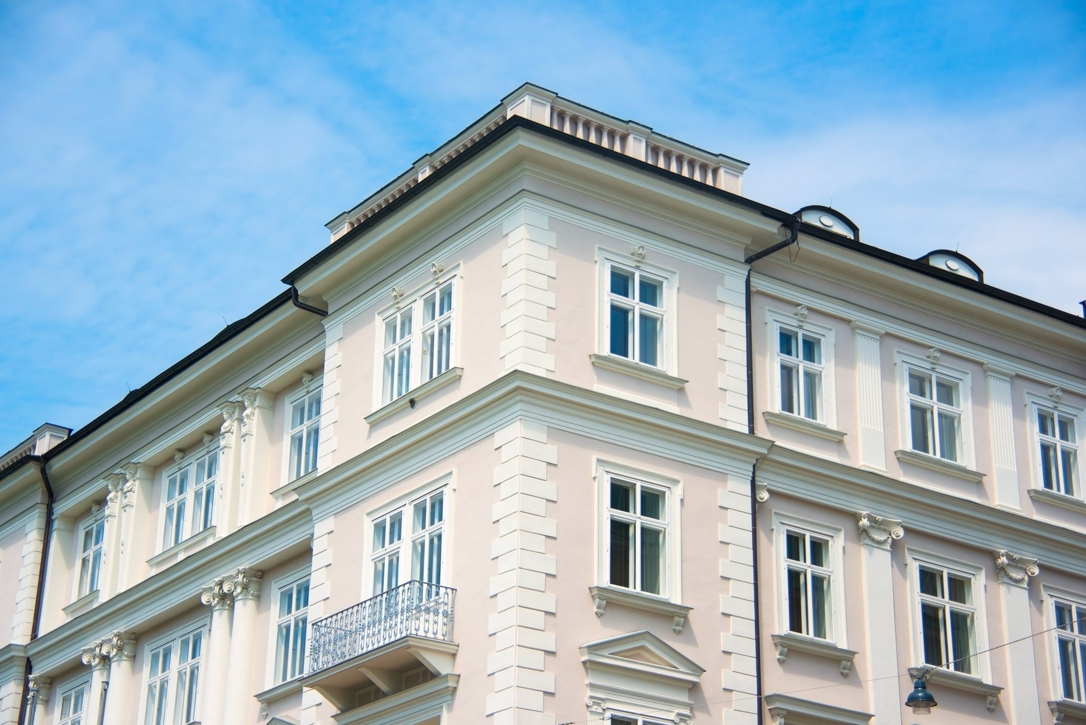 Ein mehrstöckiges, historisches Gebäude mit weißen Fassaden, vielen großen Fenstern und einer dunklen Dachkante gegen einen blauen Himmel.
