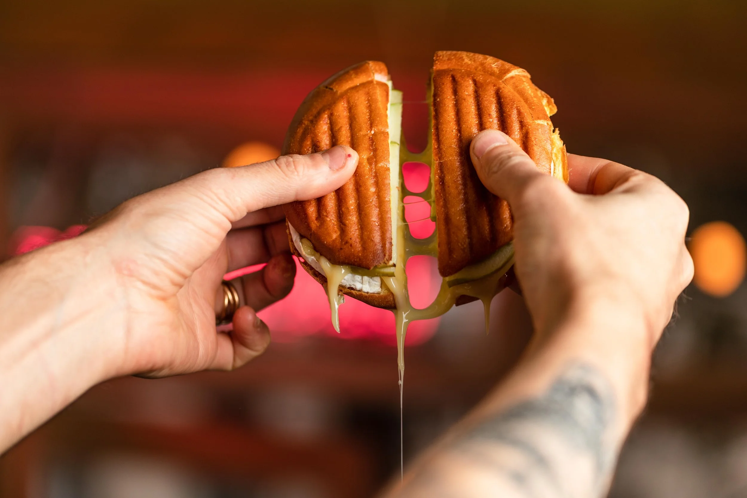 Deux mains tiennent un croque croustillant et doré rempli de fromage qui dégouline