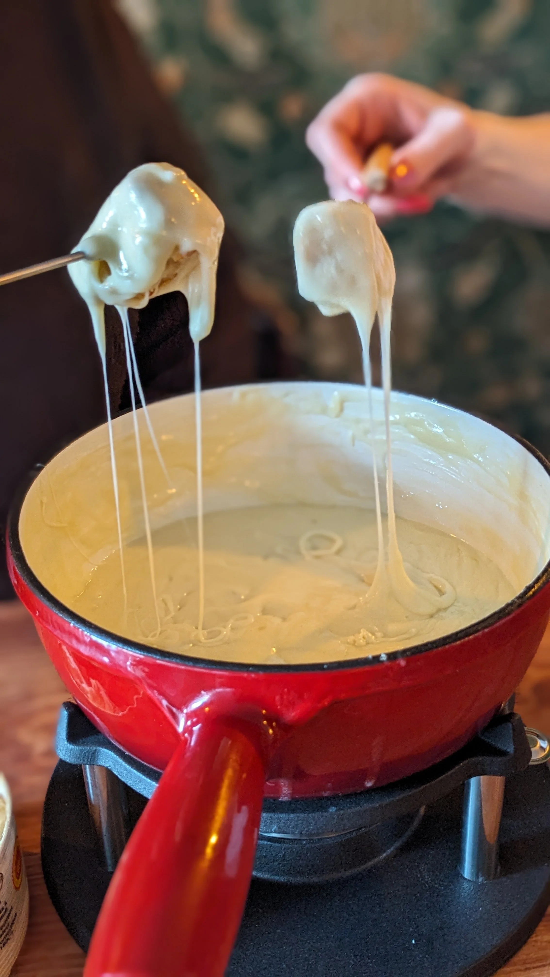 Un caquelon rouge avec de la fondue, deux personnes trempent une pain avec du fromage dans la fondue 