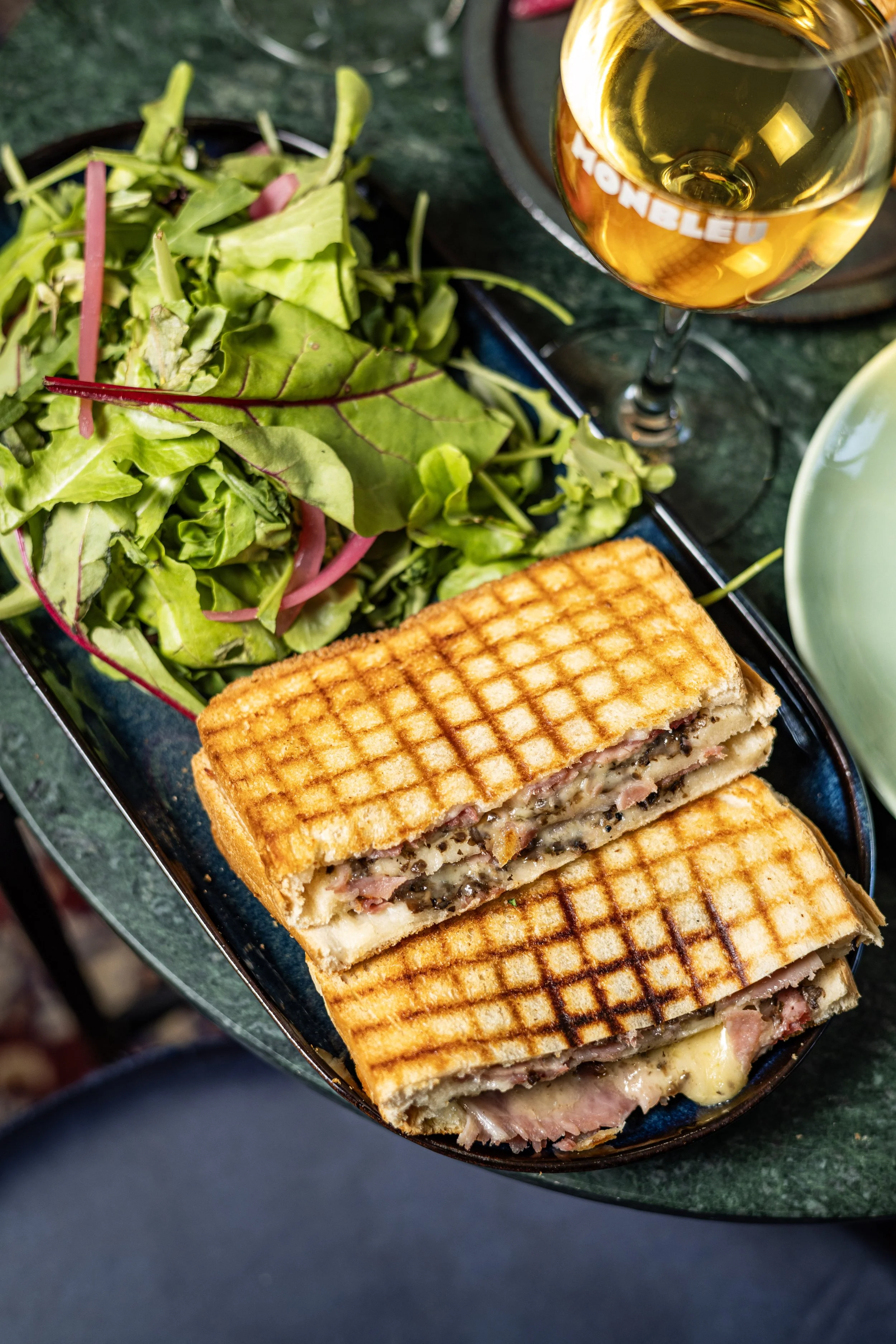 Une assiette avec un croque bien grillé et doré avec du jambon et du fromage coupé en deux, dans l'assiette il y a aussi de la salade 
