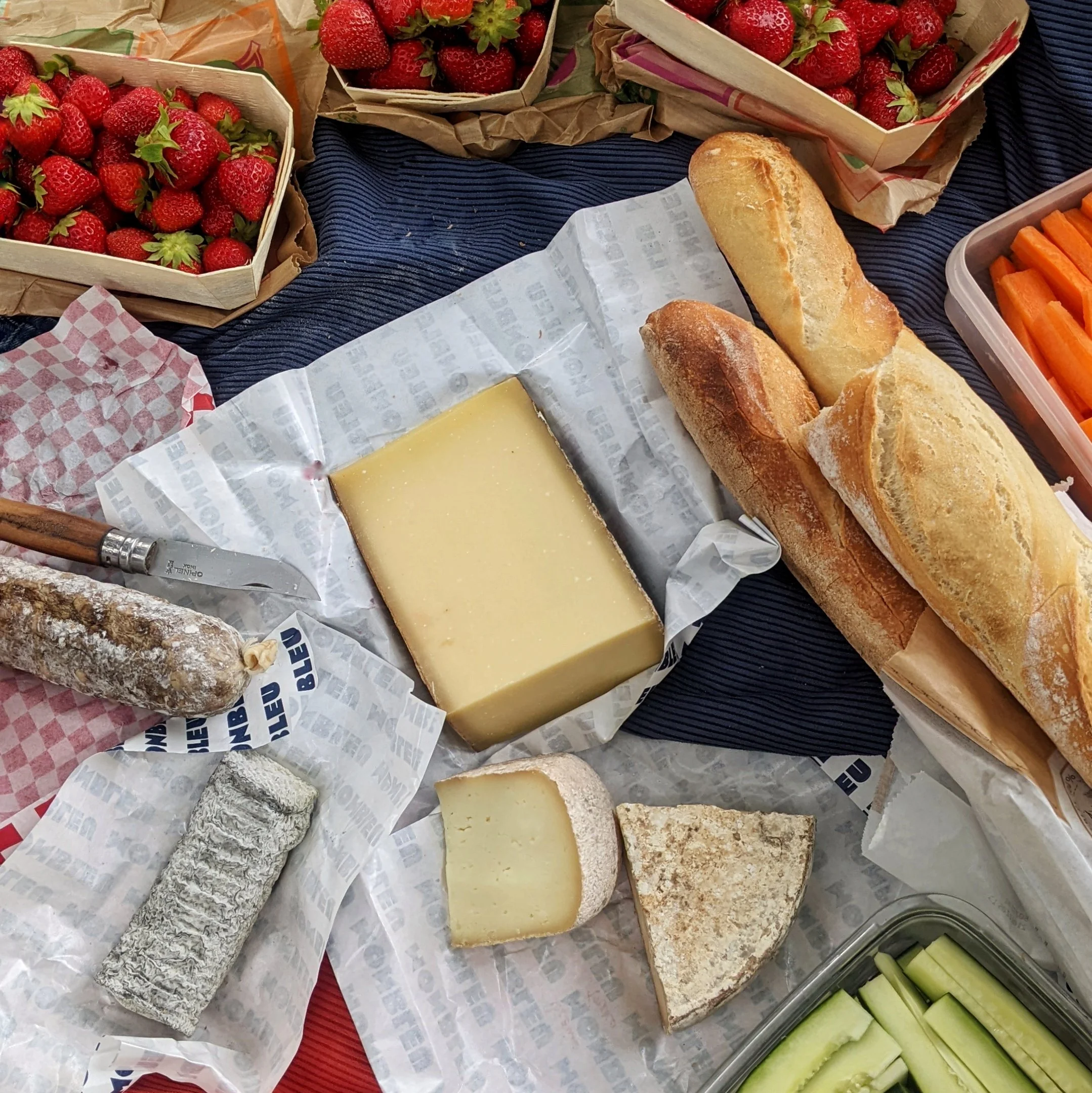 Pique-nique avec des baguettes de pain, du fromage, des fraises, de la buchette du dauphiné, des morceaux de concombres, de carottes