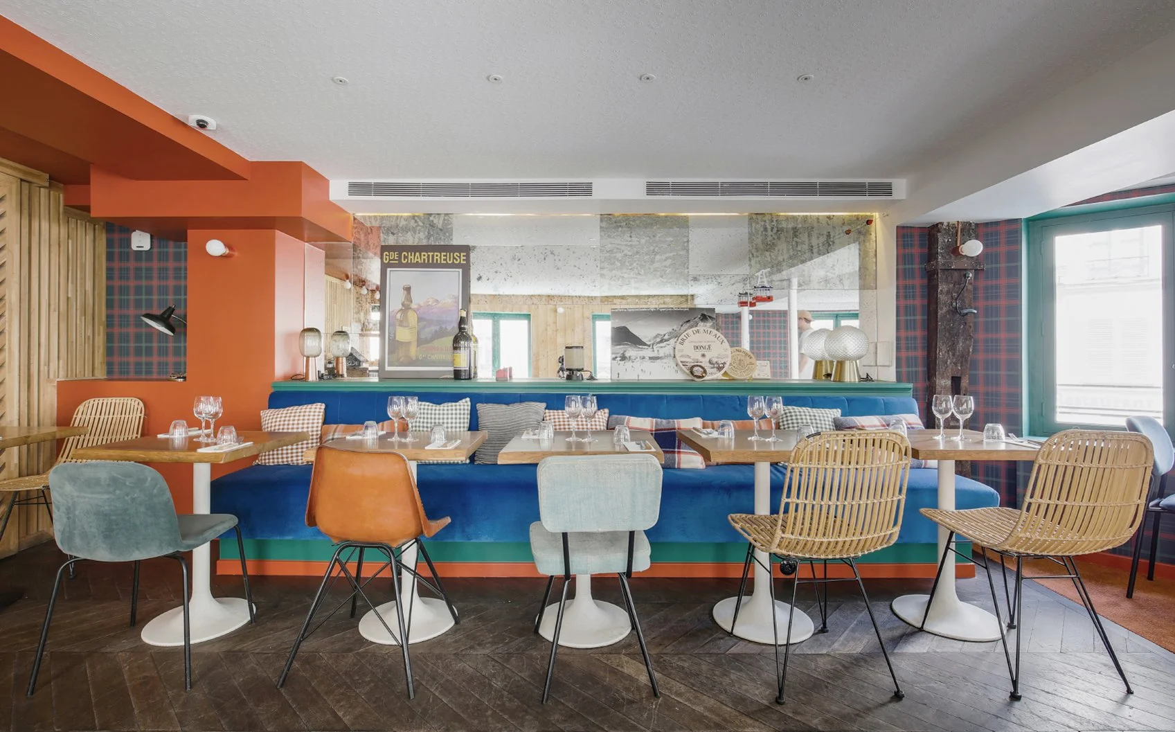 Une salle de restaurant avec plusieurs chaises et tables et un canapé bleu, il y a un grand miroir et les tables sont prêtes à accueillir des clients