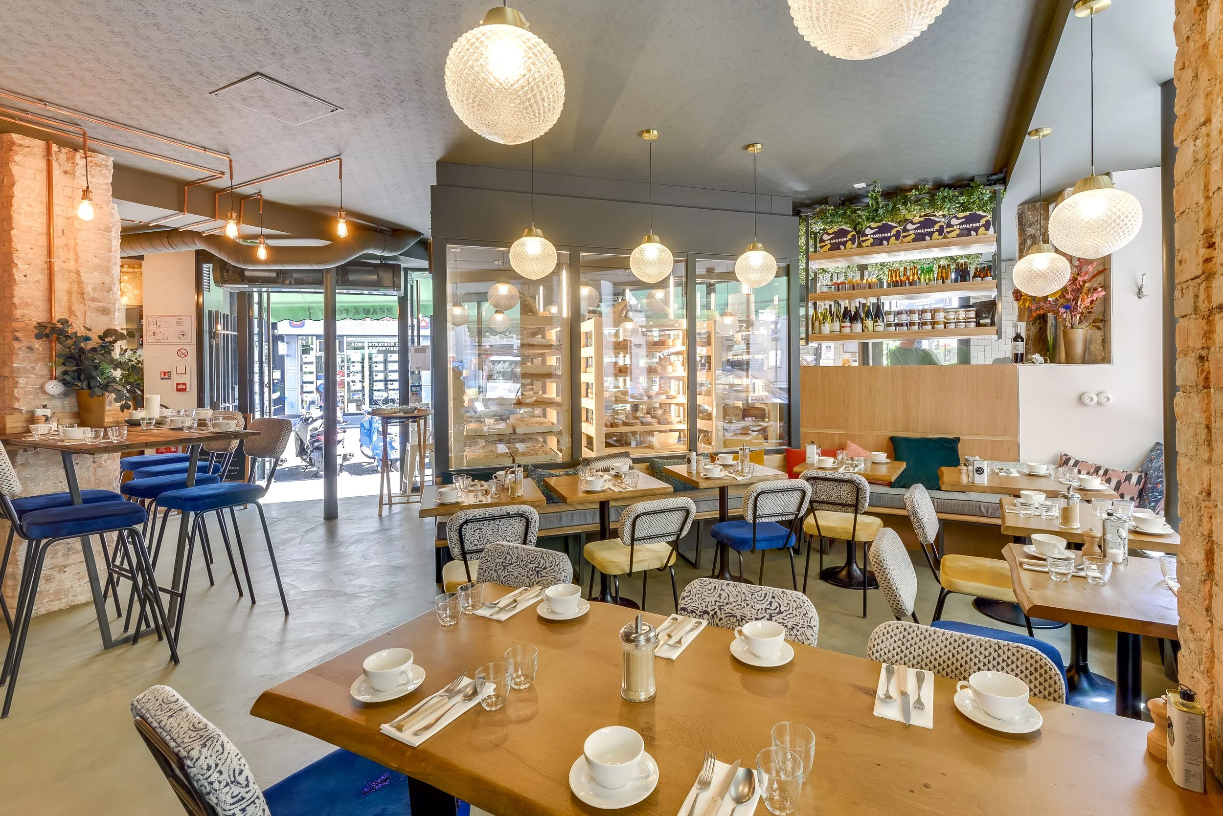 Intérieur du restaurant Monbleu Faubourg Montmartre. Plusieurs lumières en forme de boule suspendues, tables prêtes au service, chaises bleues et jaunes et grande tables en bois, intérieur très lumineux