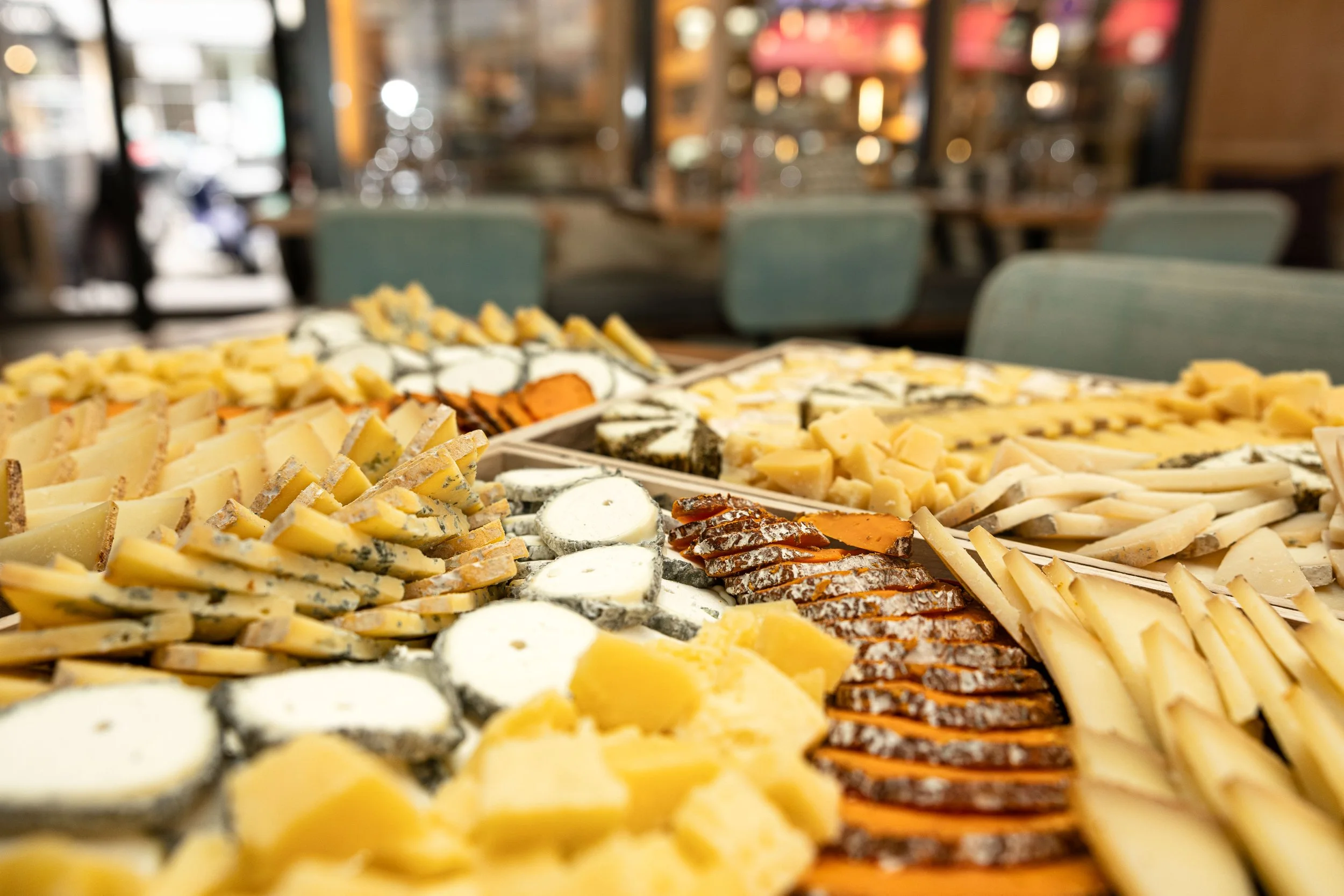 Un gros plan sur plusieurs plateaux de fromages, les couleurs sont très chaude, en arrière plan voit l'intérieur du restaurant