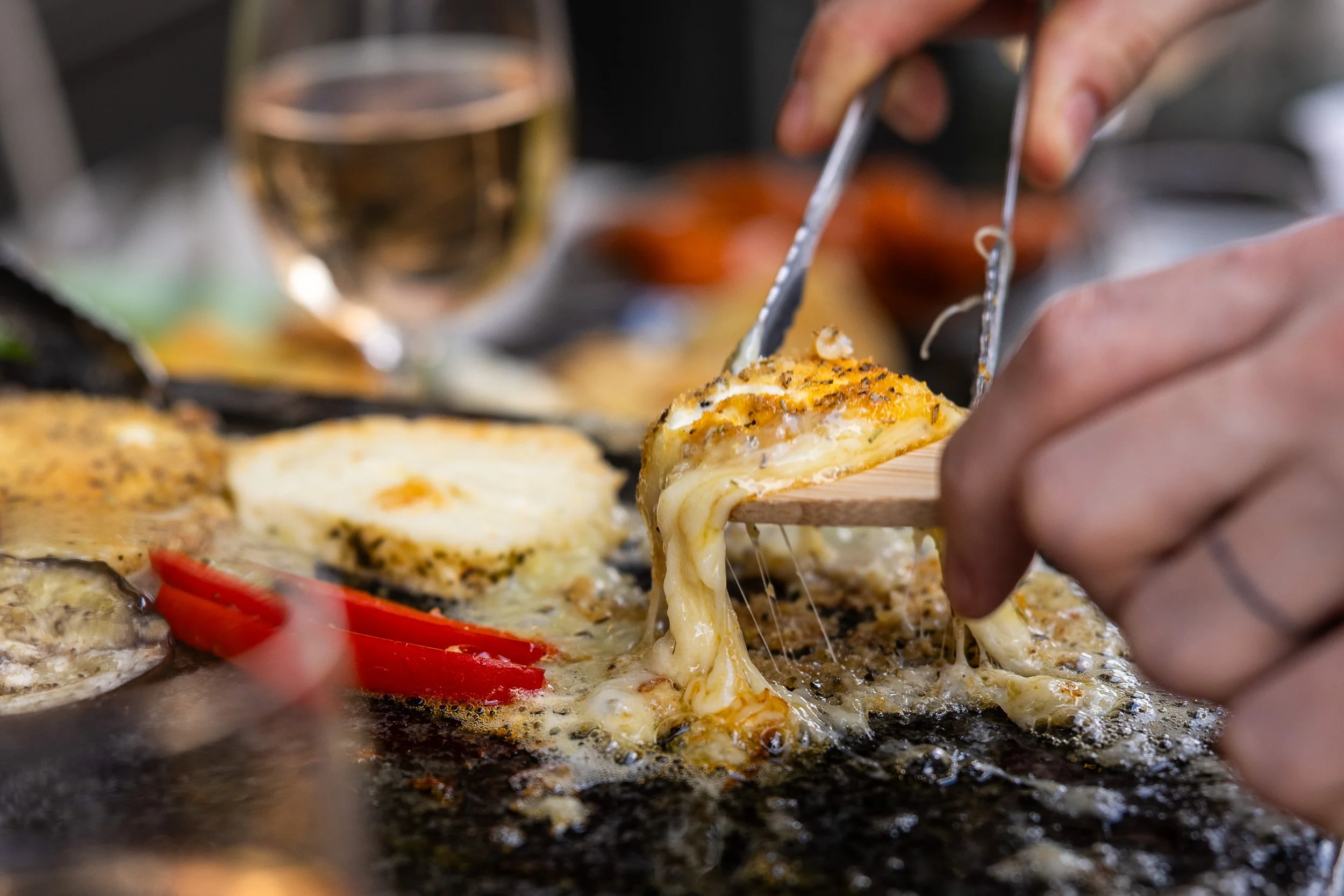 Des mains récupèrent du fromage grillé à la plancha avec une pince et une spatule