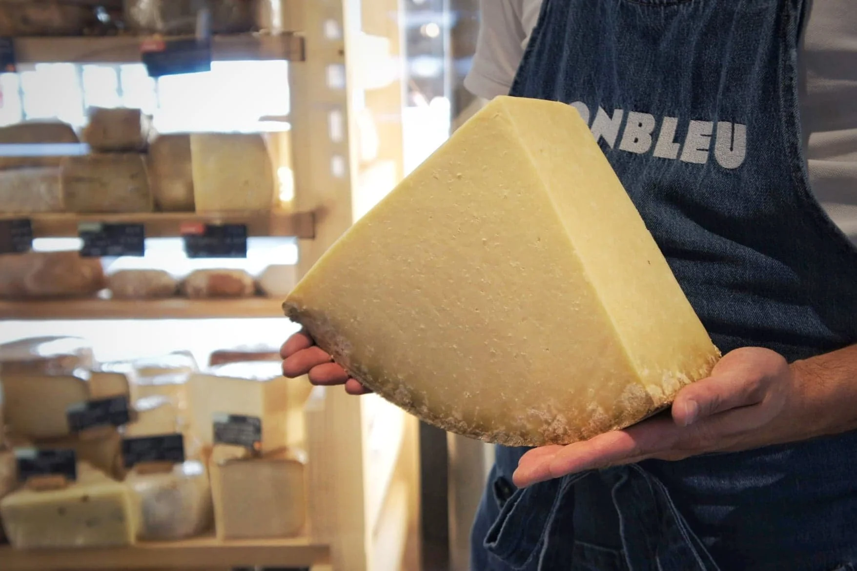 un gros fromage coupé en triangle posé dans les mains d'un fromage vêtu du tablier monbleu