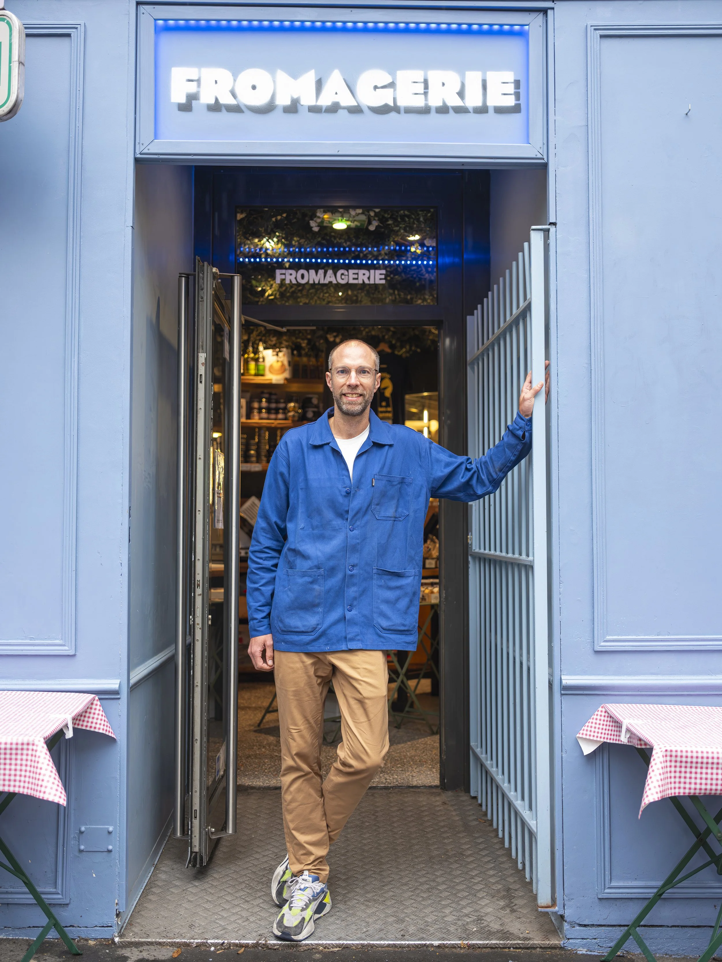 Damien richardot le fondateur des restaurants monbleu pose devant son restaurant avec une chemise bleu pétante et un pantalon marron, la façade du restaurant est bleue.
