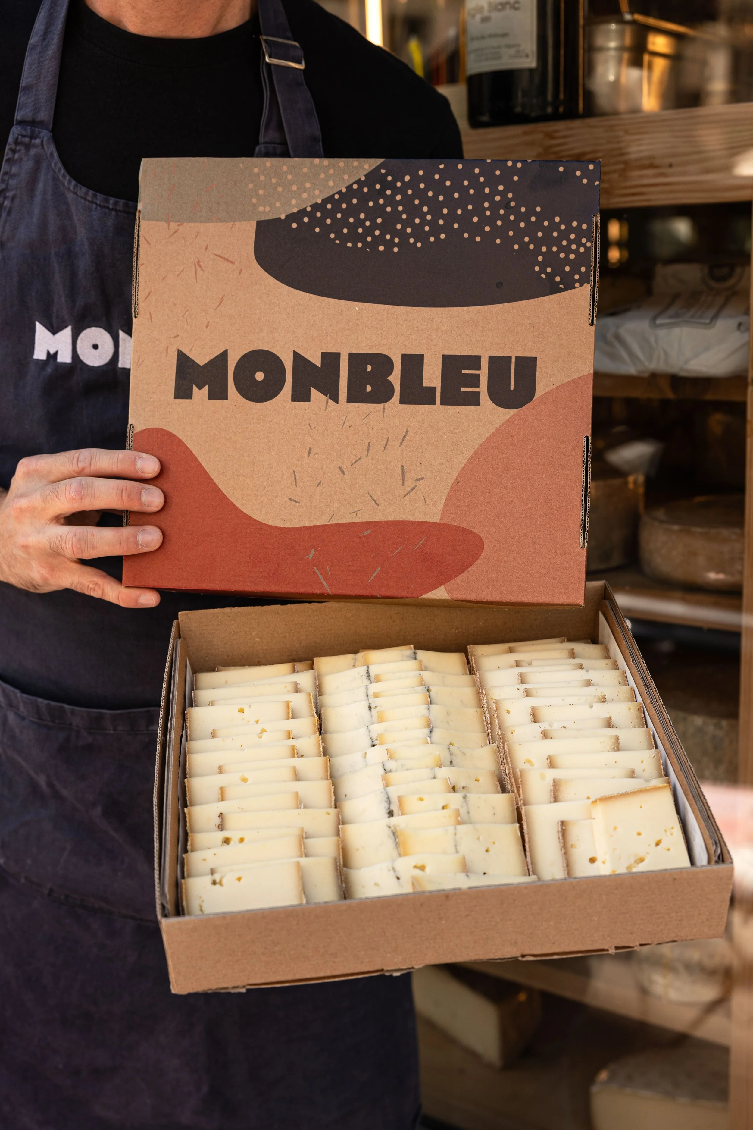 Une personne tient un plateau de fromage à raclette et dans son autre main elle tient le couvercle avec écrit "monbleu" le nom du restaurant
