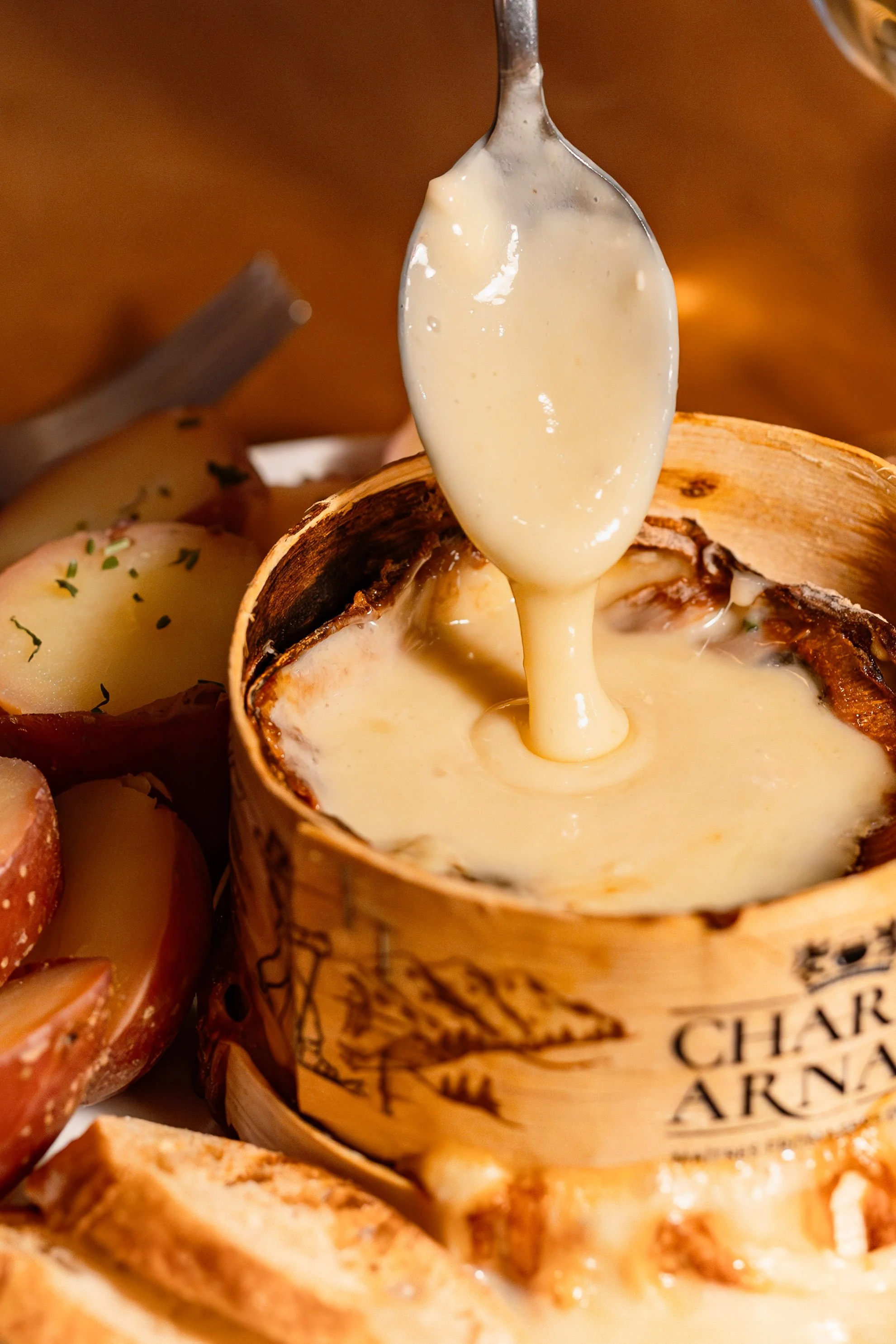 Gros plan sur un mont d'or, une cuillière est au dessus du mont d'or rempli de fromage coulant