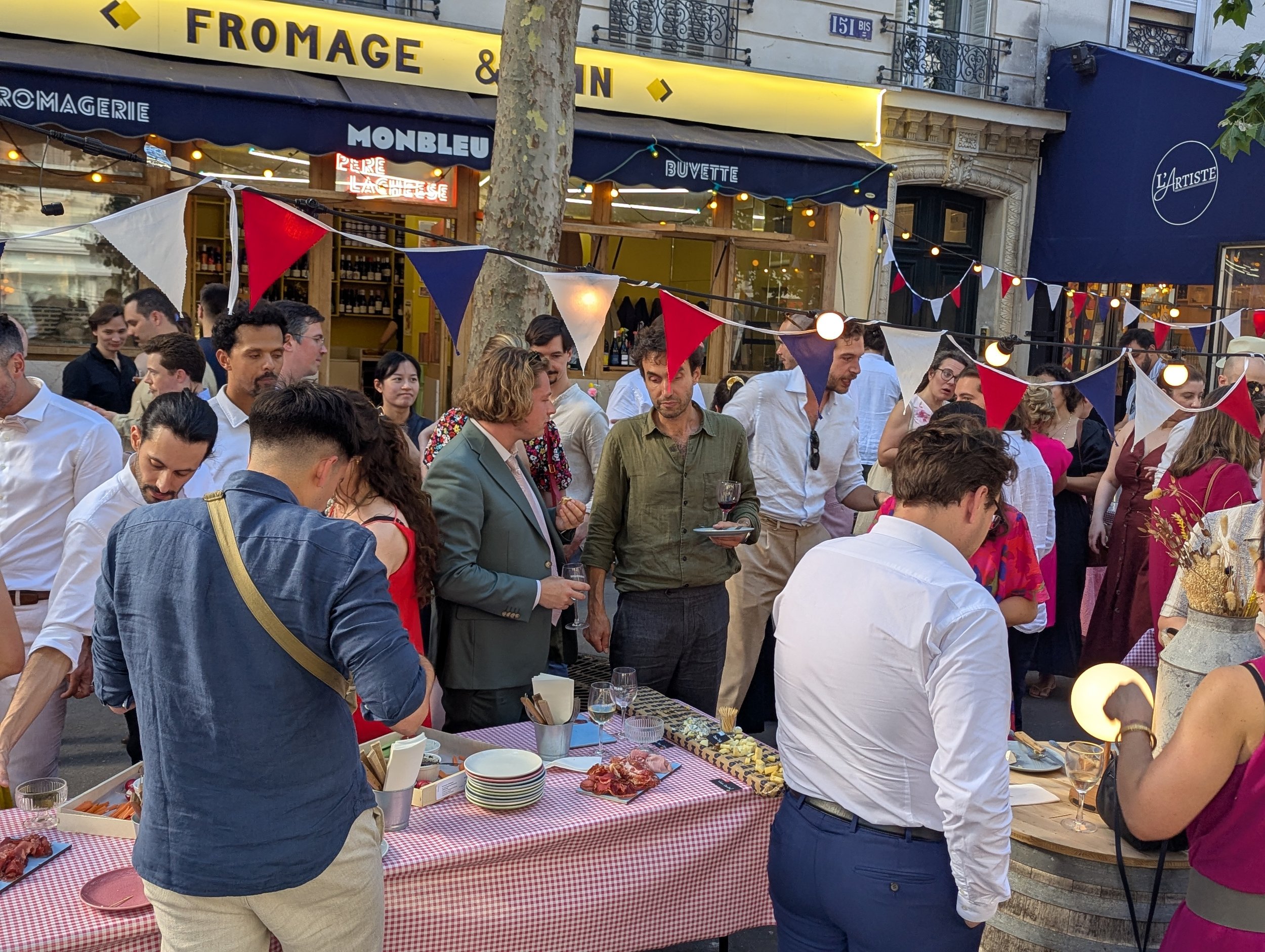 Privatisation de Monbleu père lacheese. Grande guirlande bleue, rouge et blanche, de nombreuses personnes sont debout autour des tables sur la terasse de père lacheese. 