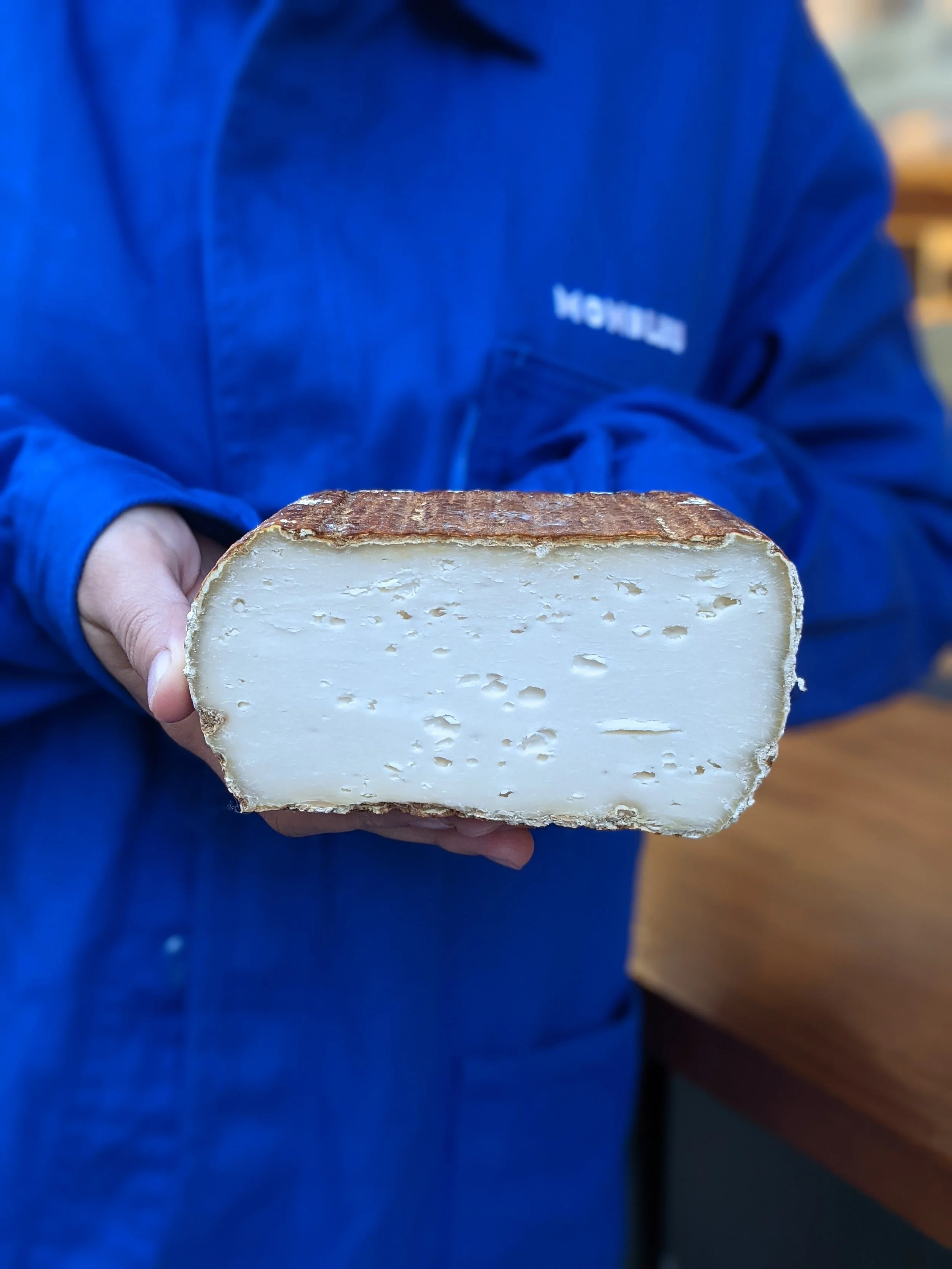 Un fromage coupé en deux est montré par un de nos fromager habillé en veste bleu avec écrit monbleu dessus. L'intérieur du fromage est très blanc