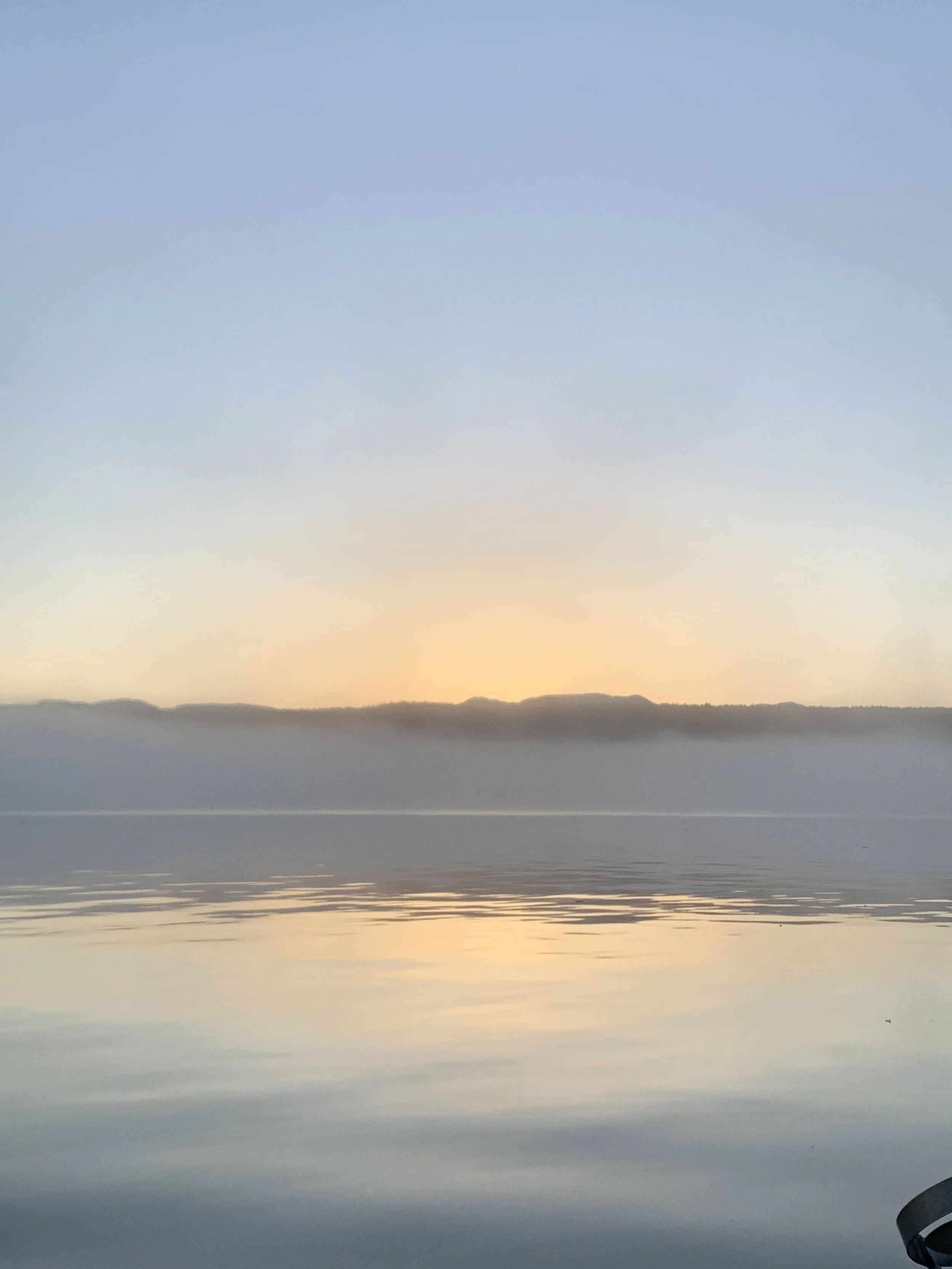A scenic view of a calm body of water with distant hills or mountains under a clear sky at sunset or sunrise.