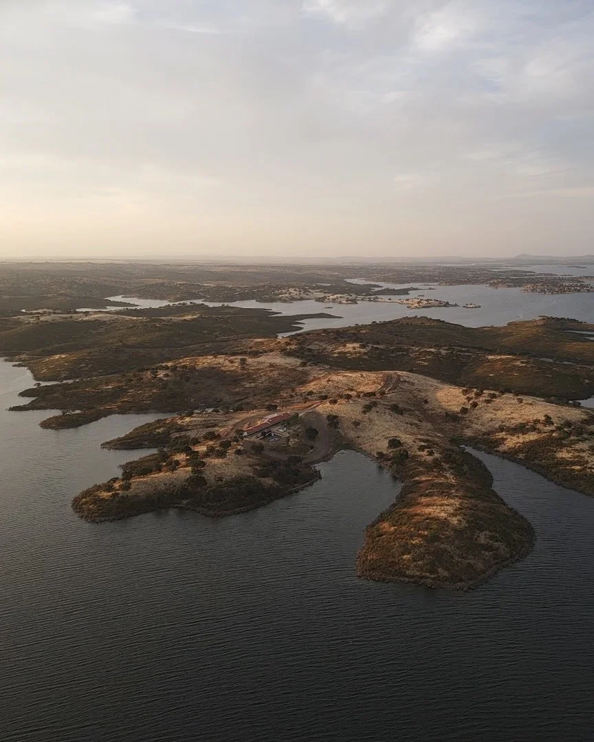 Aerial view of a landscape with water bodies, small islands, and land patches with sparse vegetation under a cloudy sky.