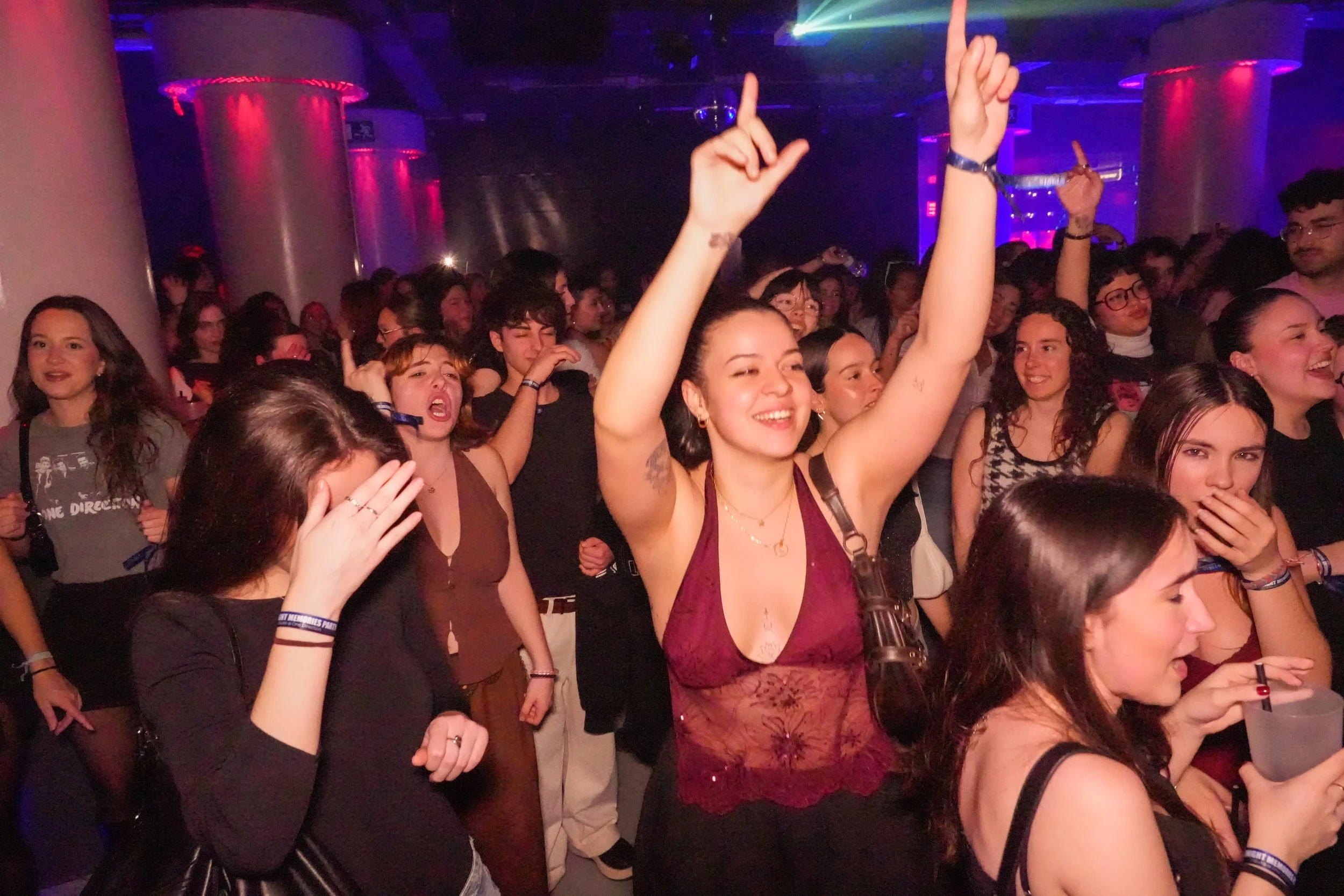 Crowd of young people dancing and enjoying themselves at a party or concert with colorful lighting.