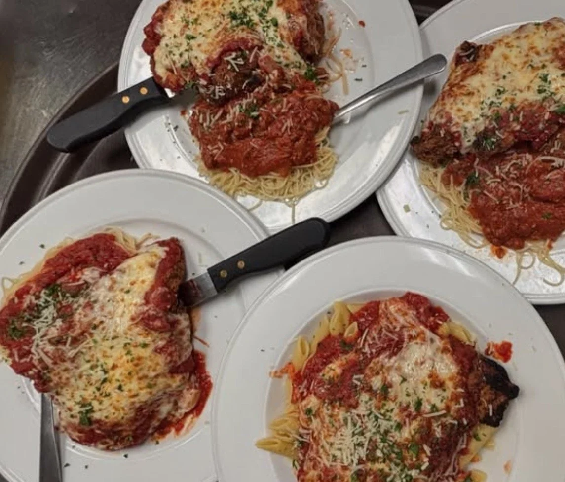 Four plates of spaghetti with meatballs, marinara sauce, and melted cheese garnished with parsley on a tray.