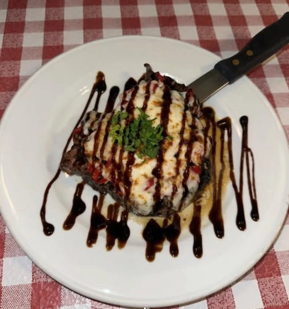 Slice of cake topped with whipped cream, chocolate syrup, and a sprig of cilantro on a white plate with additional chocolate drizzle, on a checkered tablecloth.