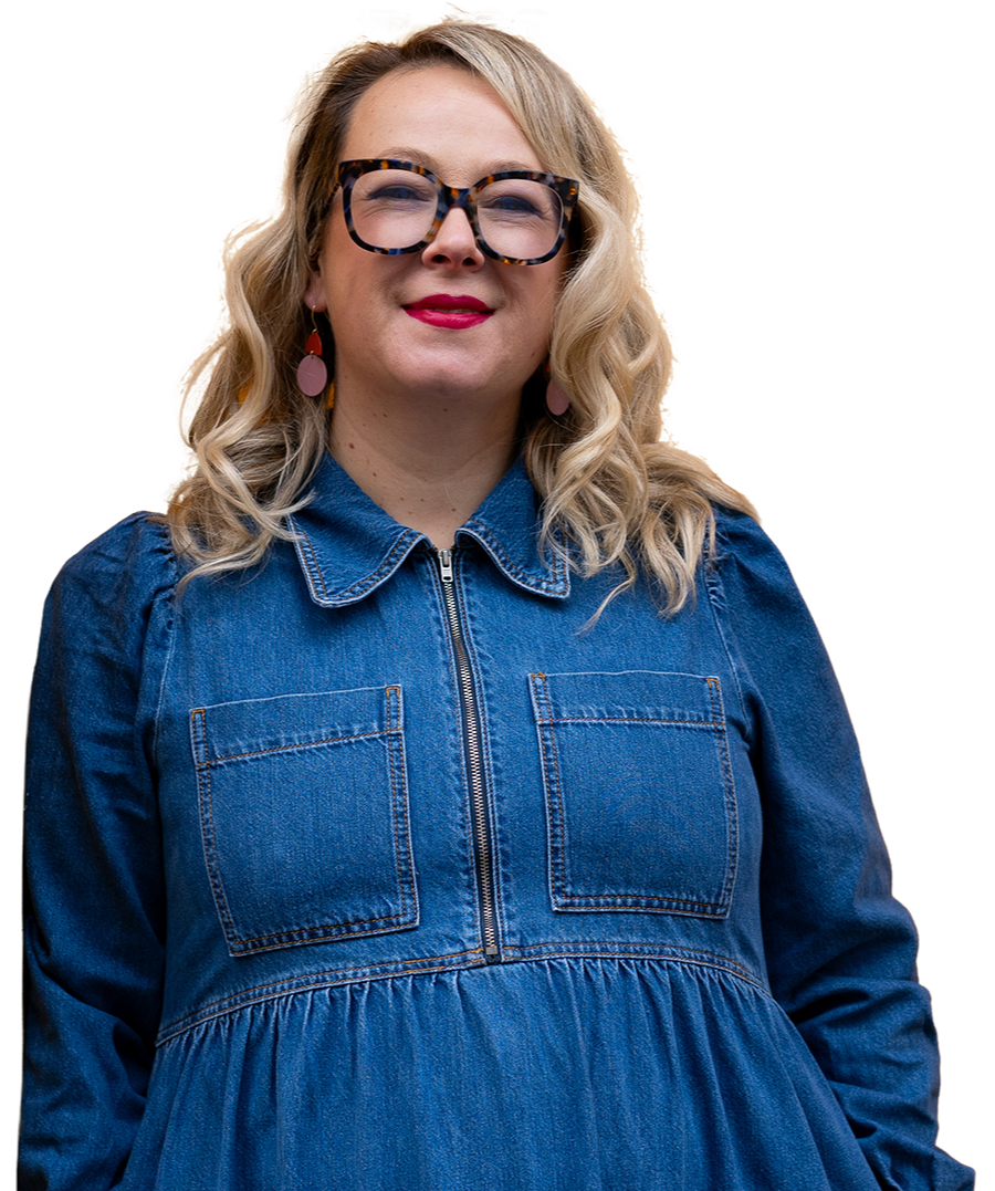 A woman with blonde curly hair wearing glasses, pink earrings, red lipstick, and a denim dress.