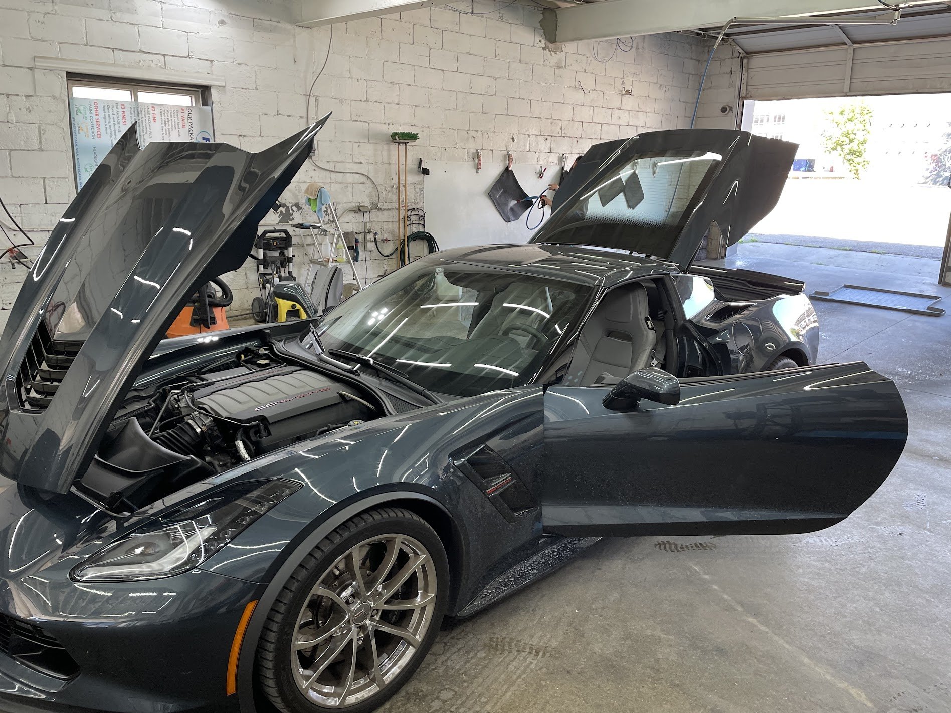 A dark gray sports car in a garage with its hood and trunk open, showcasing the engine and trunk space.