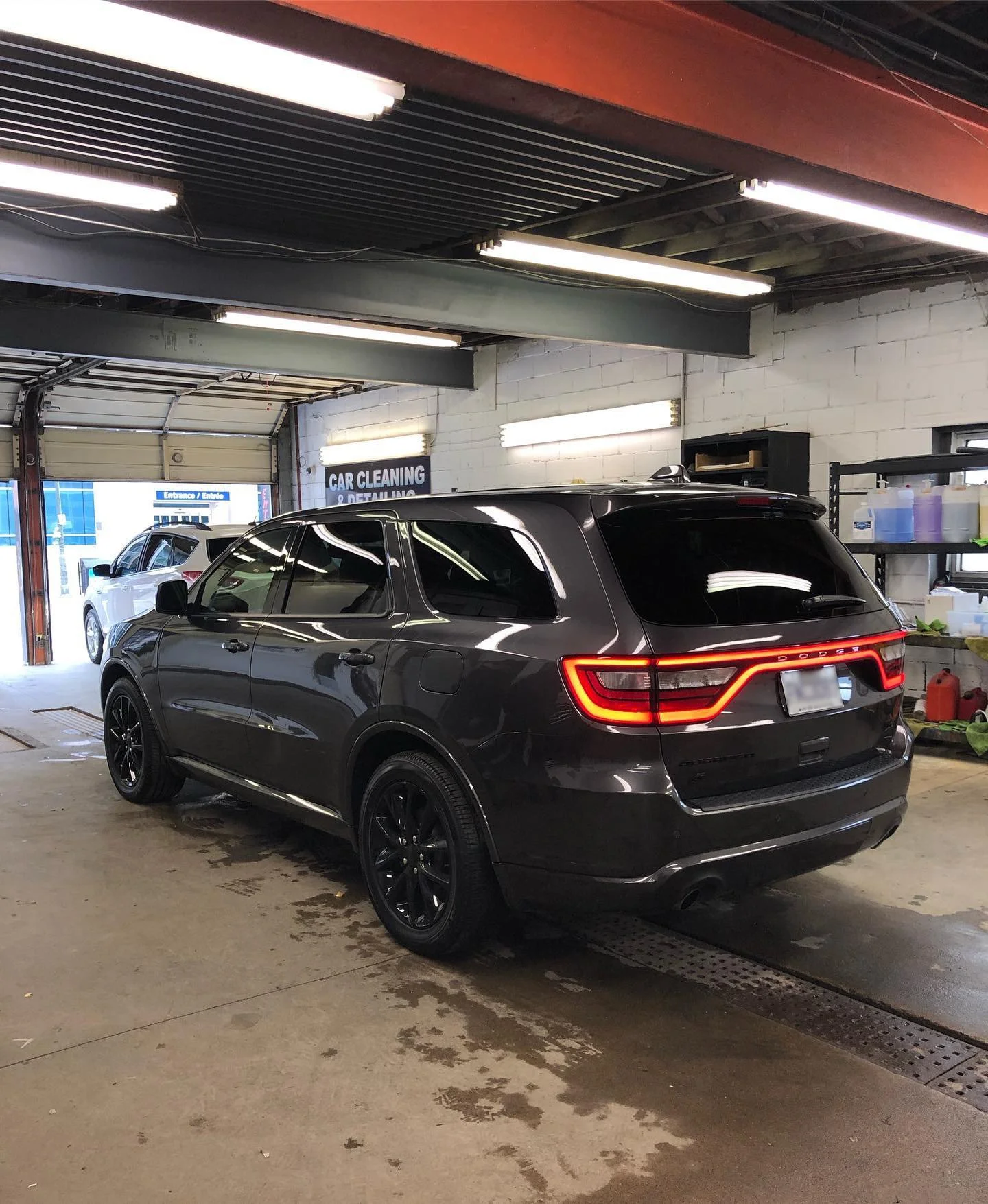 Black SUV parked inside an auto detailing garage with fluorescent lights and shelves with cleaning supplies in the background.