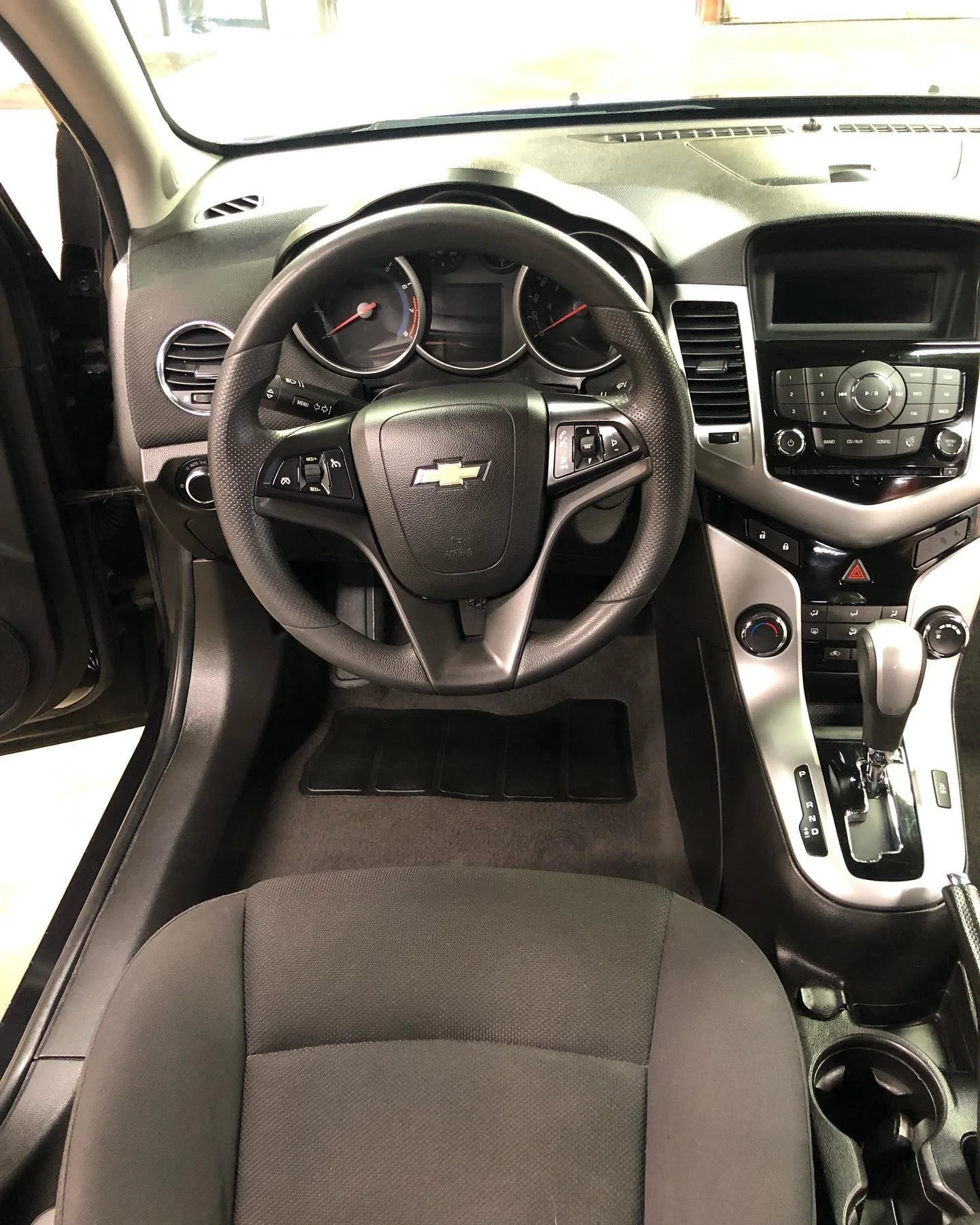 Interior view of a Chevrolet car dashboard, steering wheel, and center console, with a black and silver color scheme and visible gear shift.