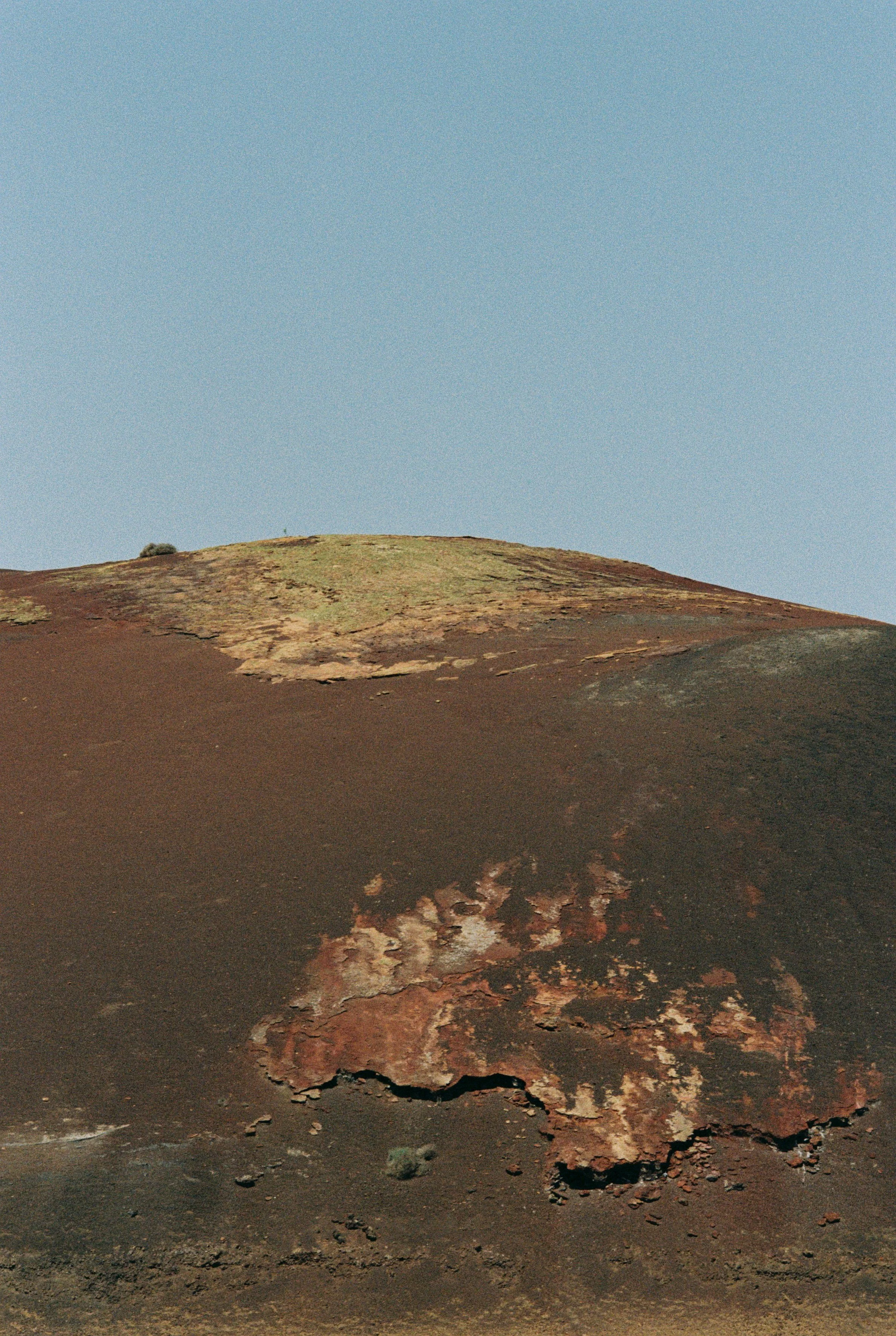 Close-up view of a rocky, weathered landscape with a hill under a clear blue sky.
