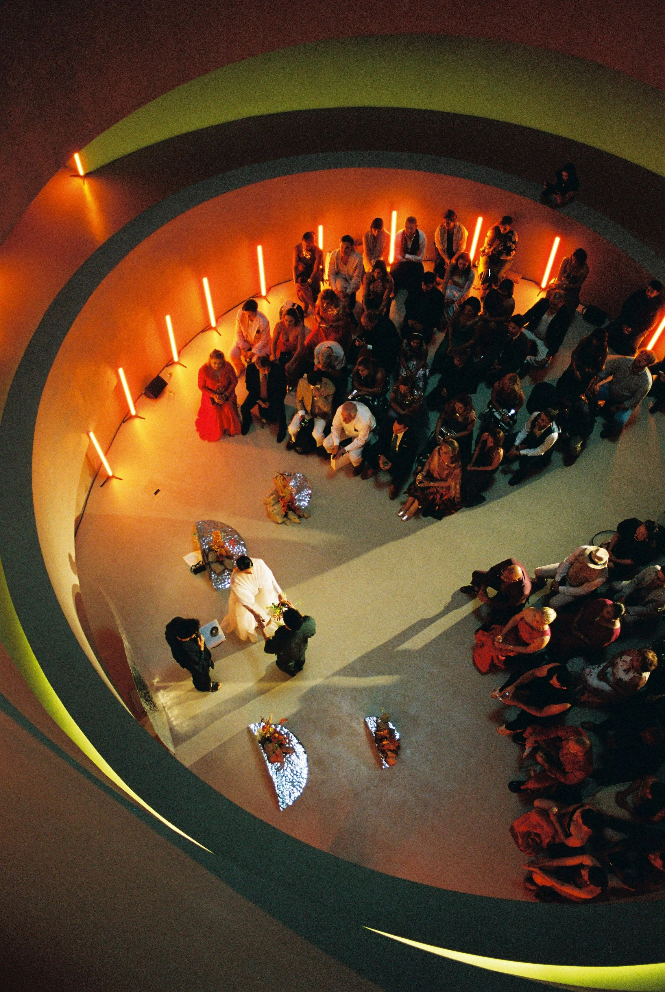 People gathered around a table in a dimly lit setting with orange lighting, seen from an aerial perspective.
