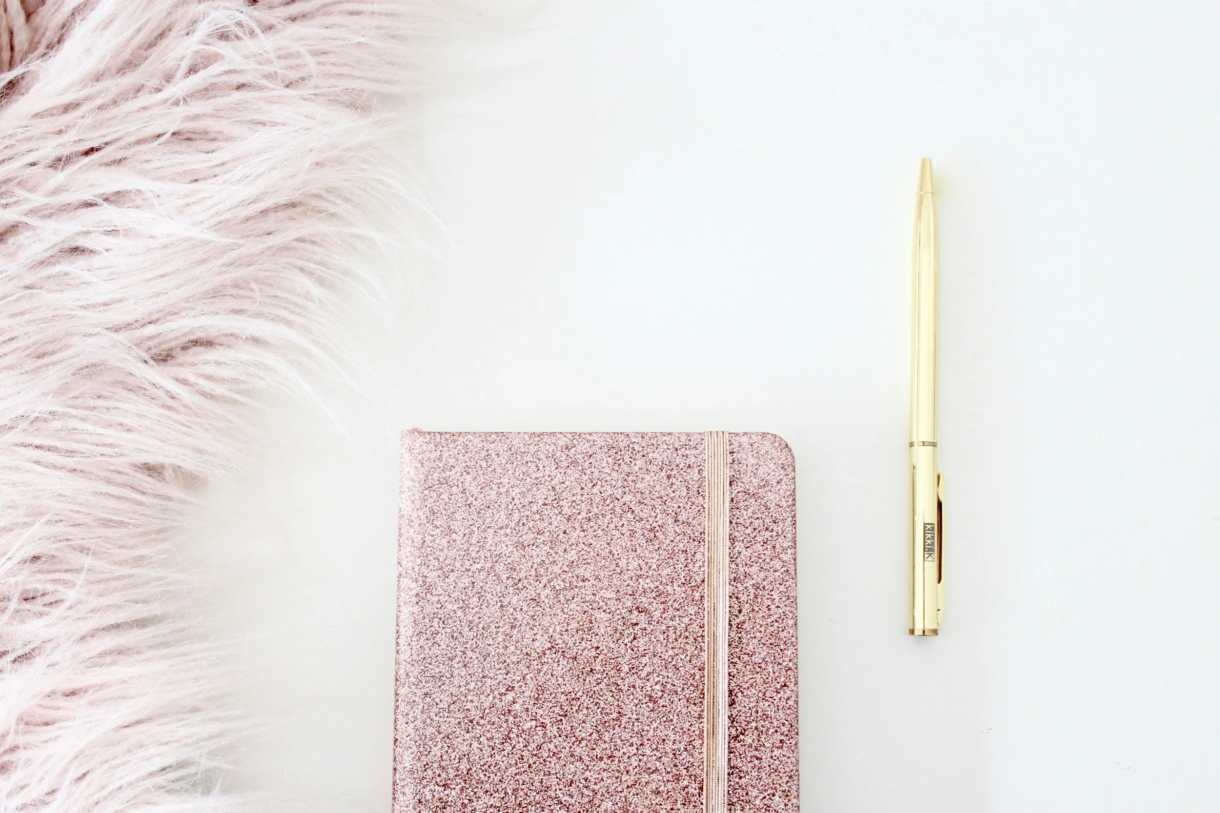 Pink notebook and gold pen on a soft, neutral background.