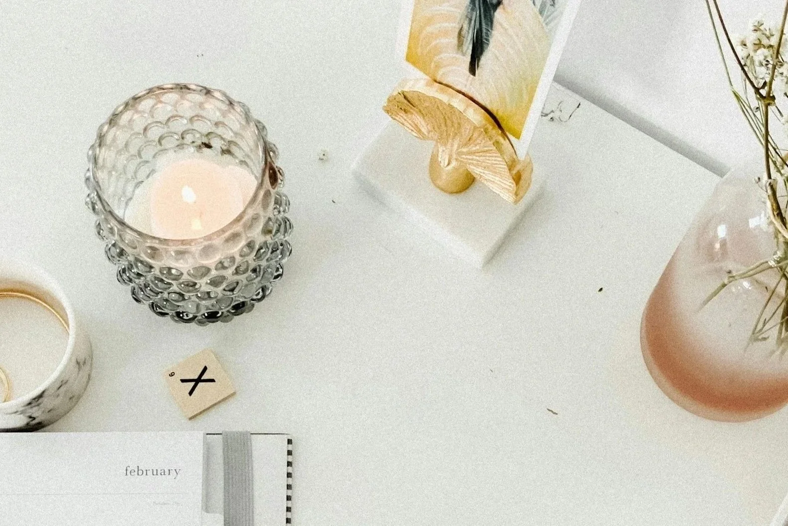 Candle, planner, and dried flowers arranged on a bright, calming workspace.