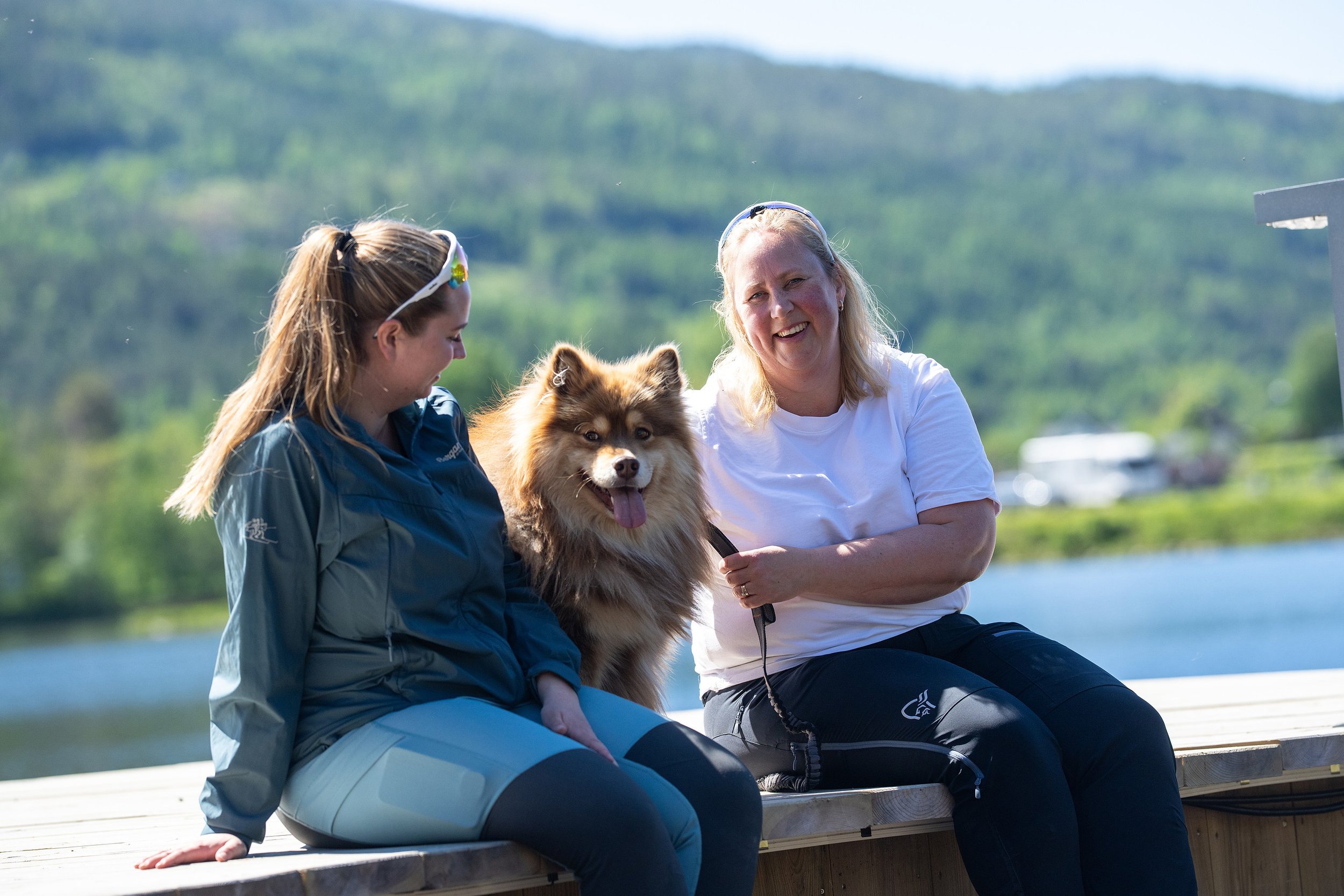 Bilde av to personer med hund på bryggekanten.