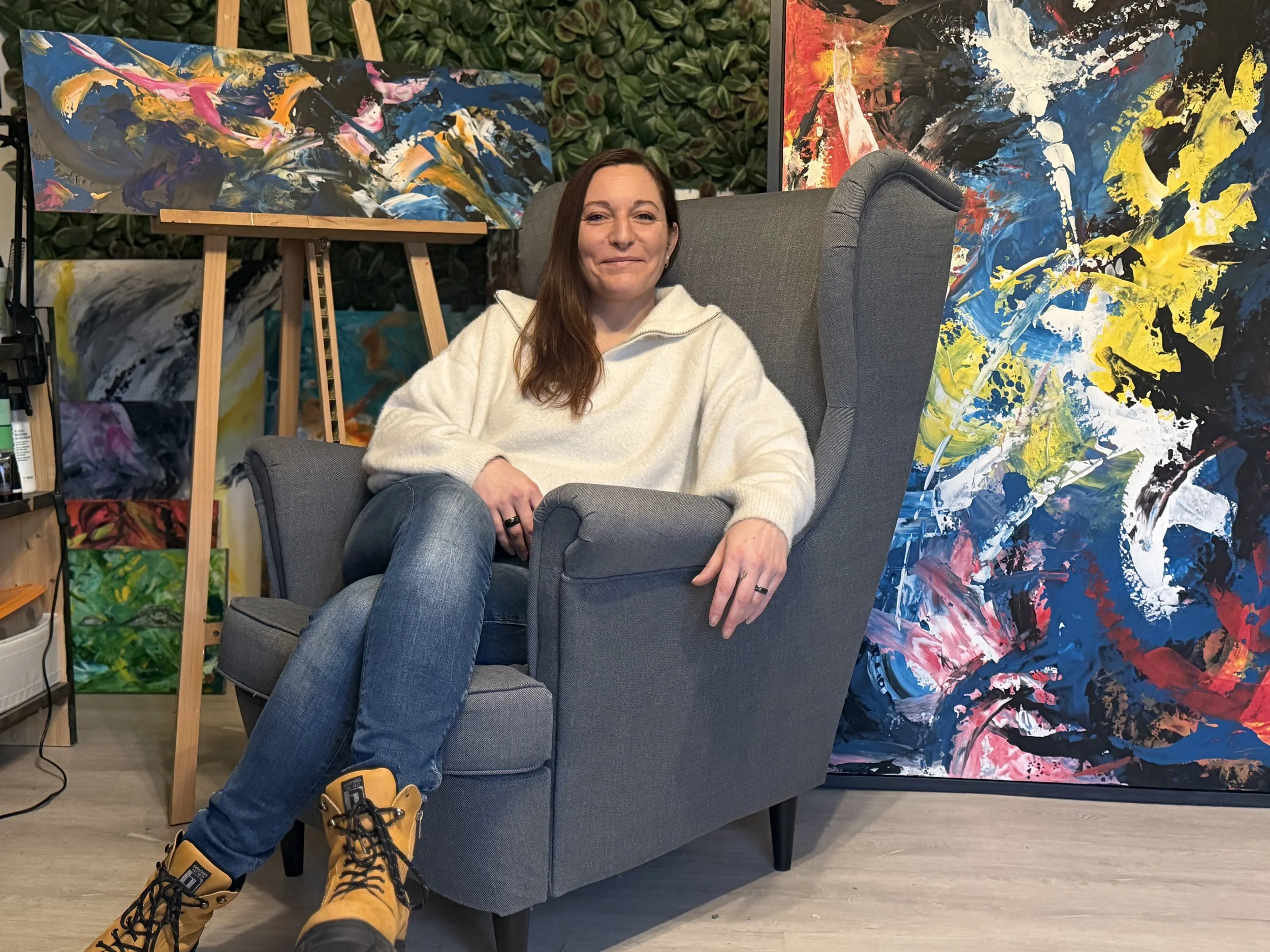 Künstlerin Anne Lilly Lippek in ihrem Atelier, umgeben von farbintensiven abstrakten Gemälden und Kunstmaterialien.