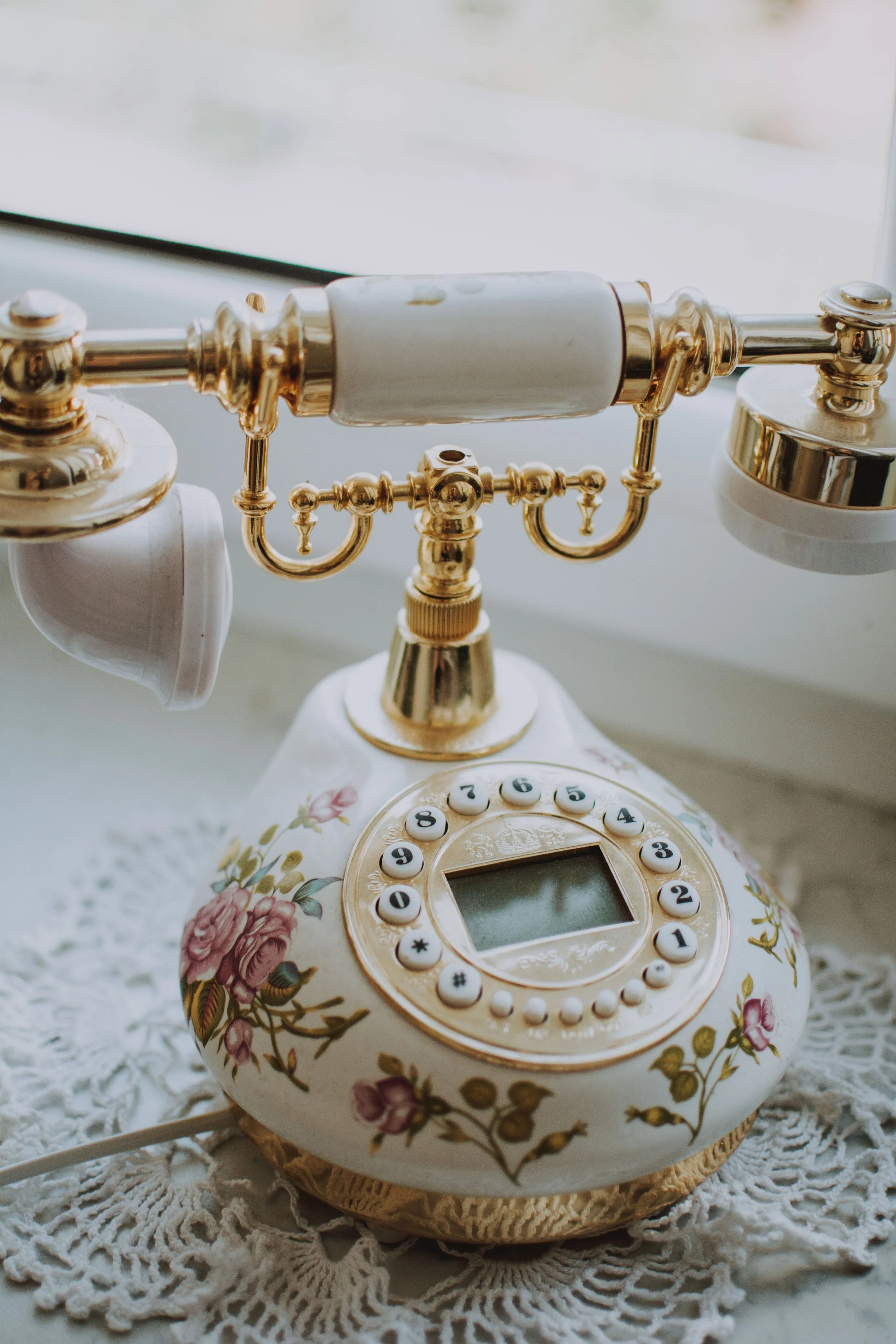An antique landline telephone with a floral pattern on the base, featuring a rotary dial with buttons and an old-fashioned handset resting on top.
