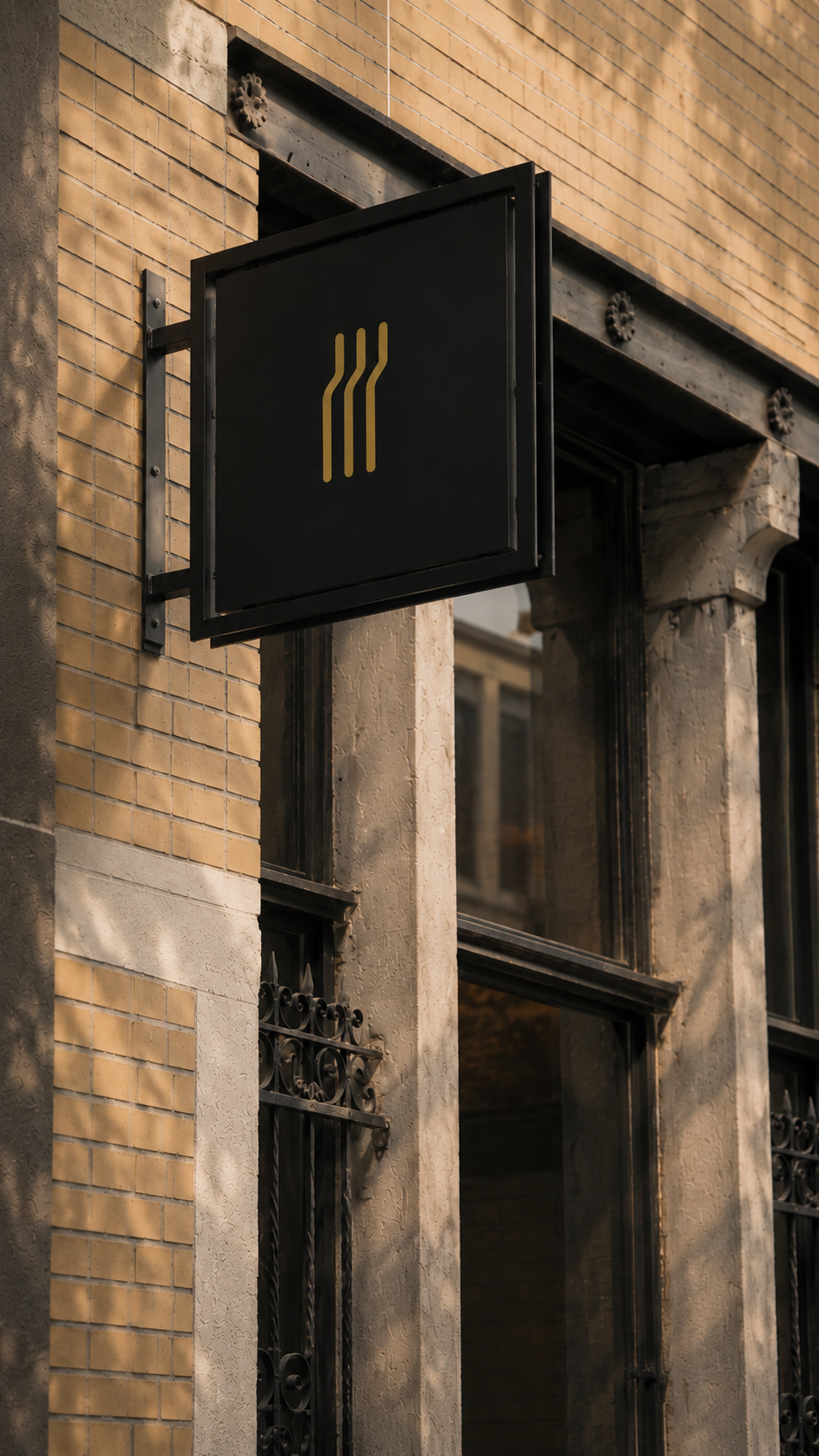 Black sign with three gold wavy lines hanging on the beige brick building exterior.