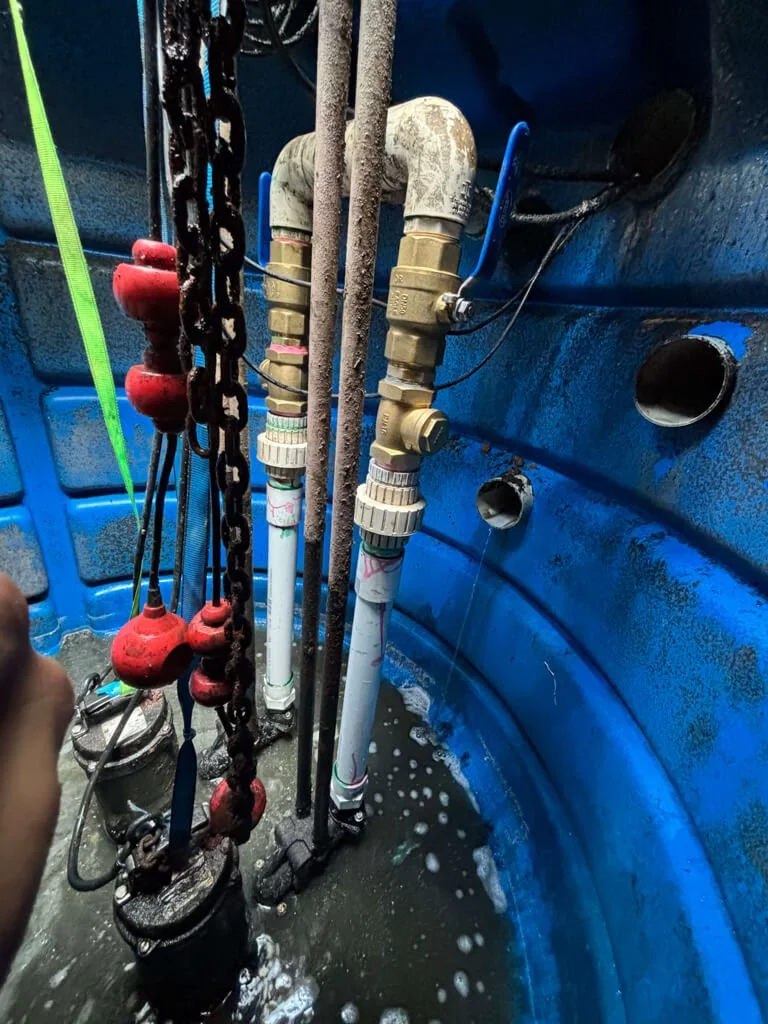 Plumbing pipes and fittings inside a blue tank or container, with water around the base and some pressure gauges and valves.