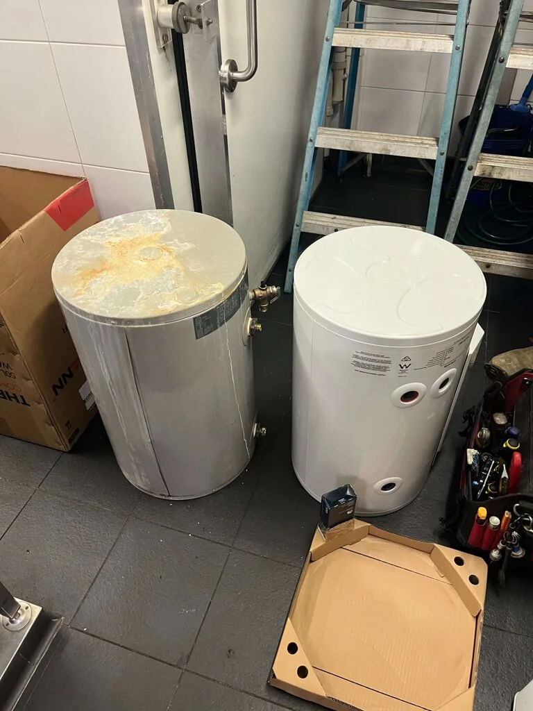 Old rusty water heater next to a new cleaned water heater in a utility room.