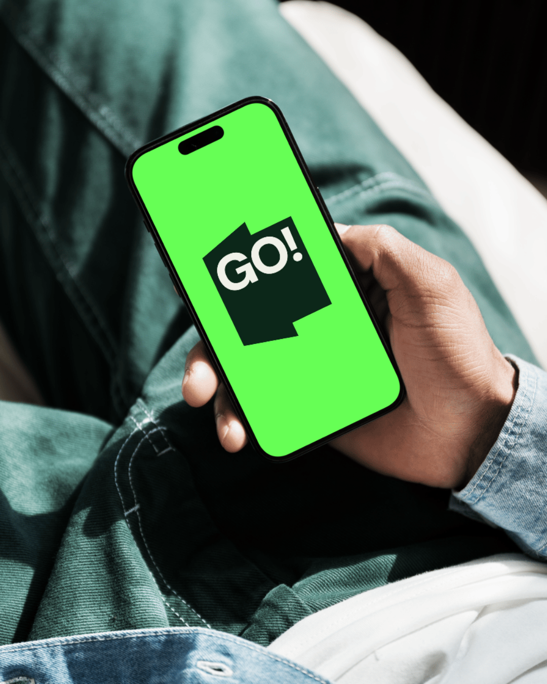 En person holder en smartphone med en grøn skærm, der viser teksten 'GO!' i sort og hvid.